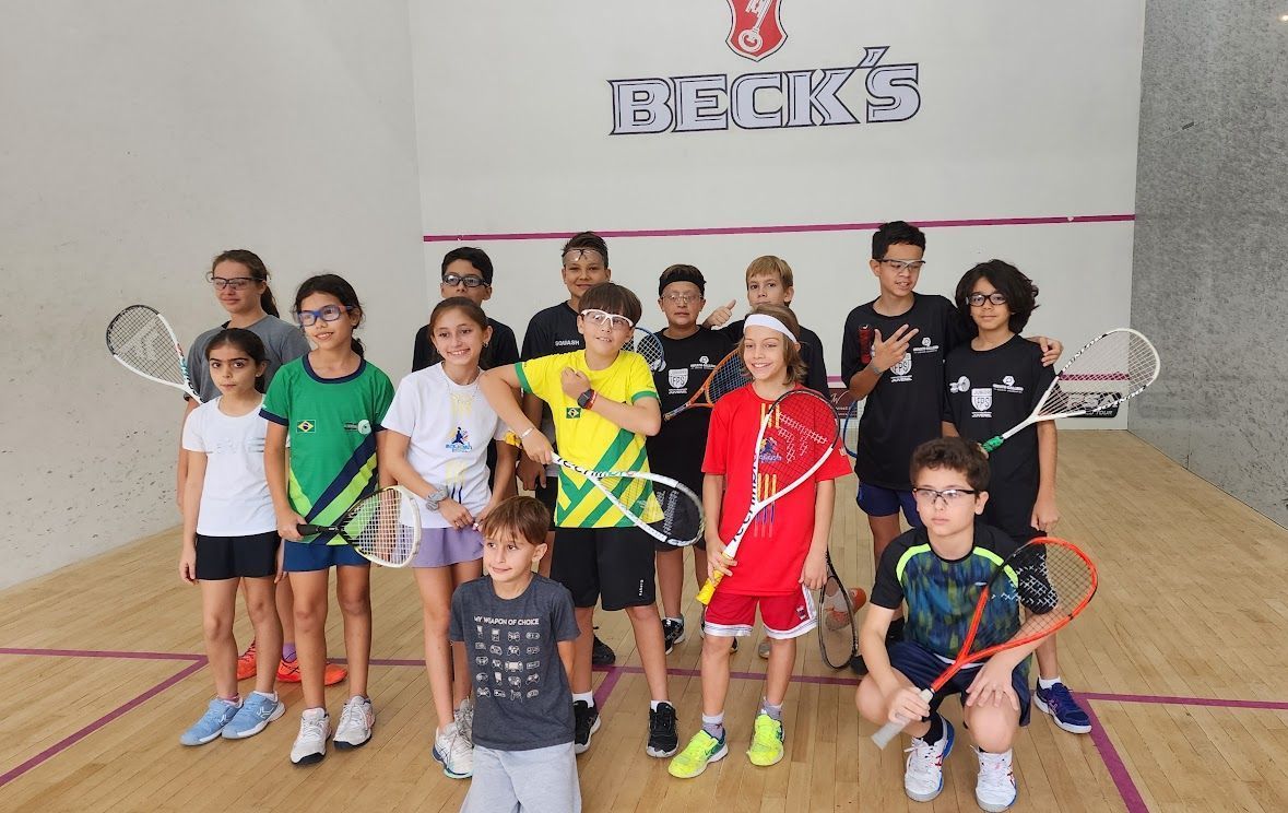 Um grupo de crianças está posando para uma foto em uma quadra de squash.