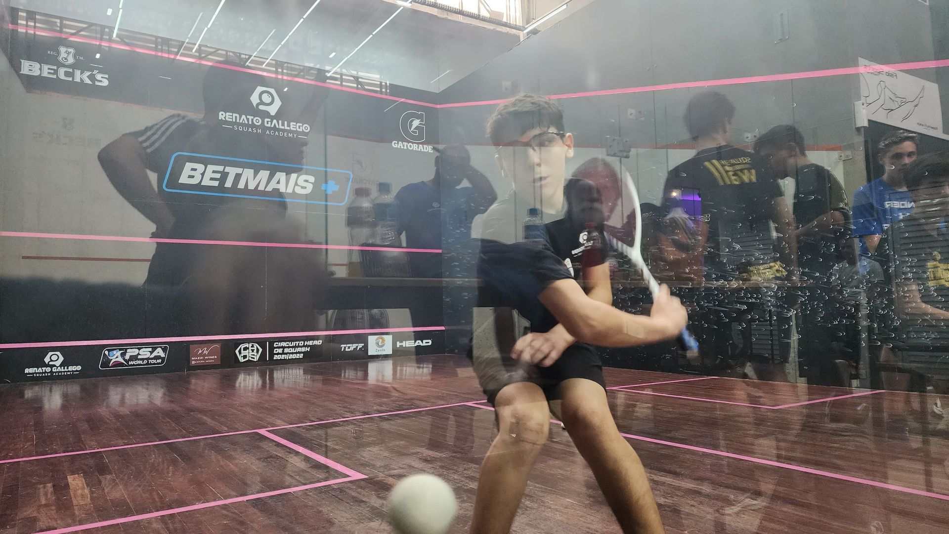 Um homem está jogando squash em uma quadra na frente de uma multidão.