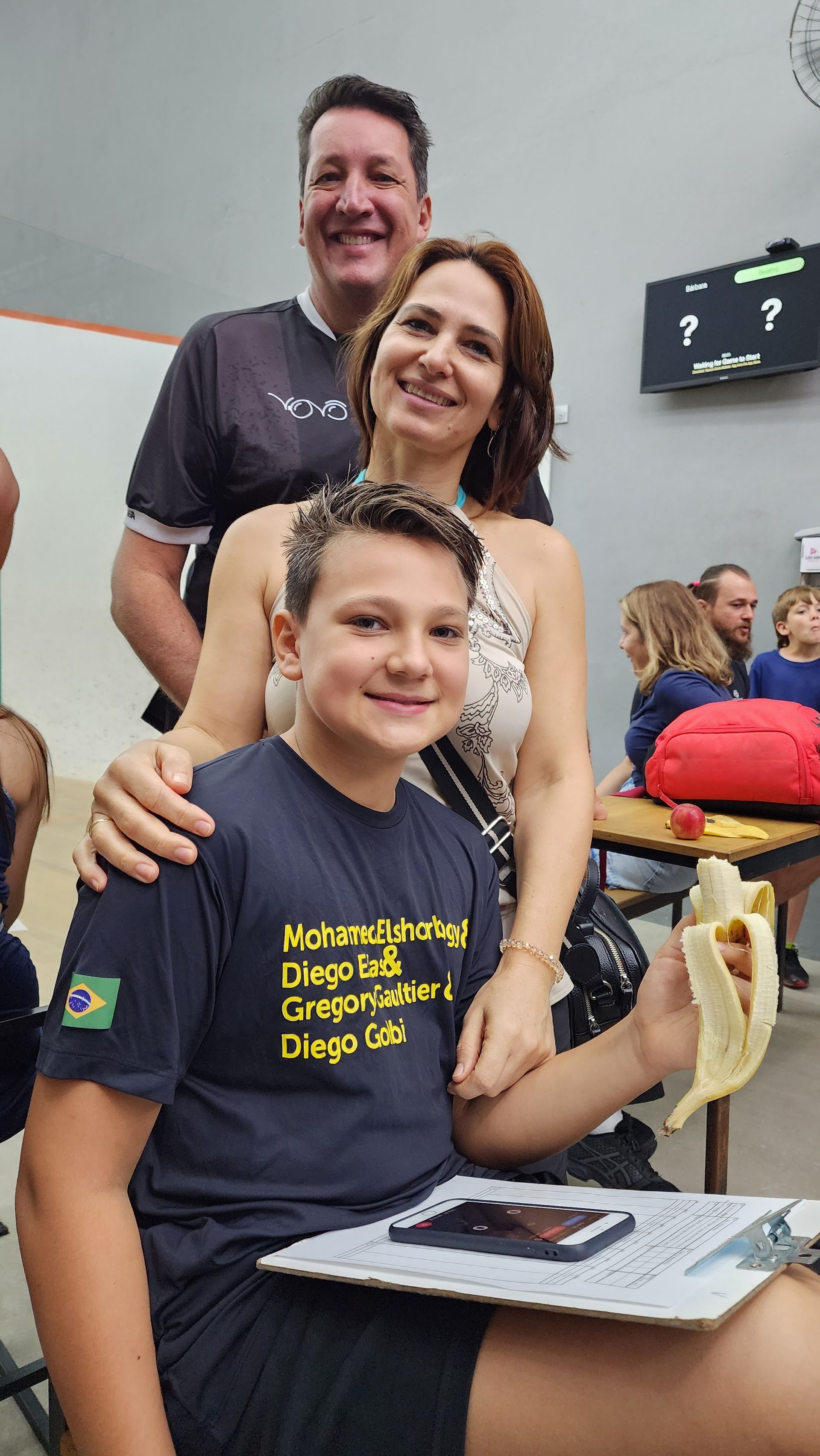 um homem e uma mulher estão ao lado de um menino segurando uma banana.