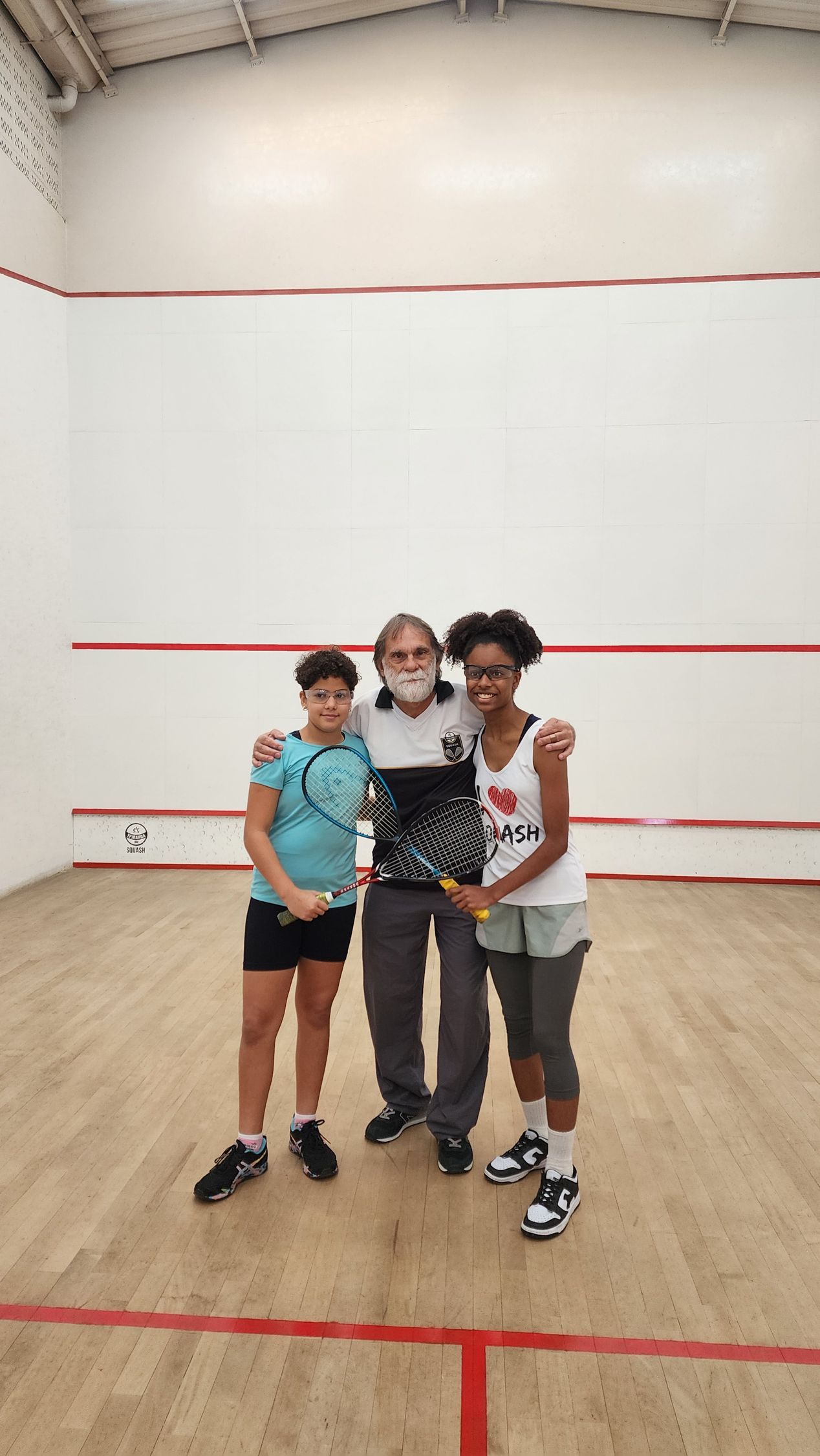 Três pessoas estão posando para uma foto em uma quadra de squash.