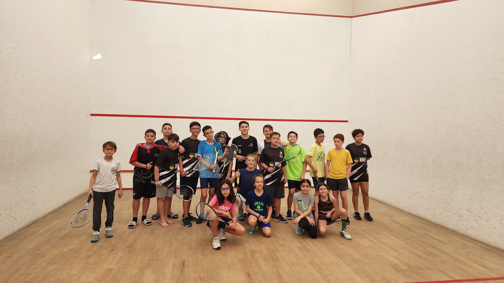 Um grupo de pessoas está posando para uma foto em uma quadra de squash.