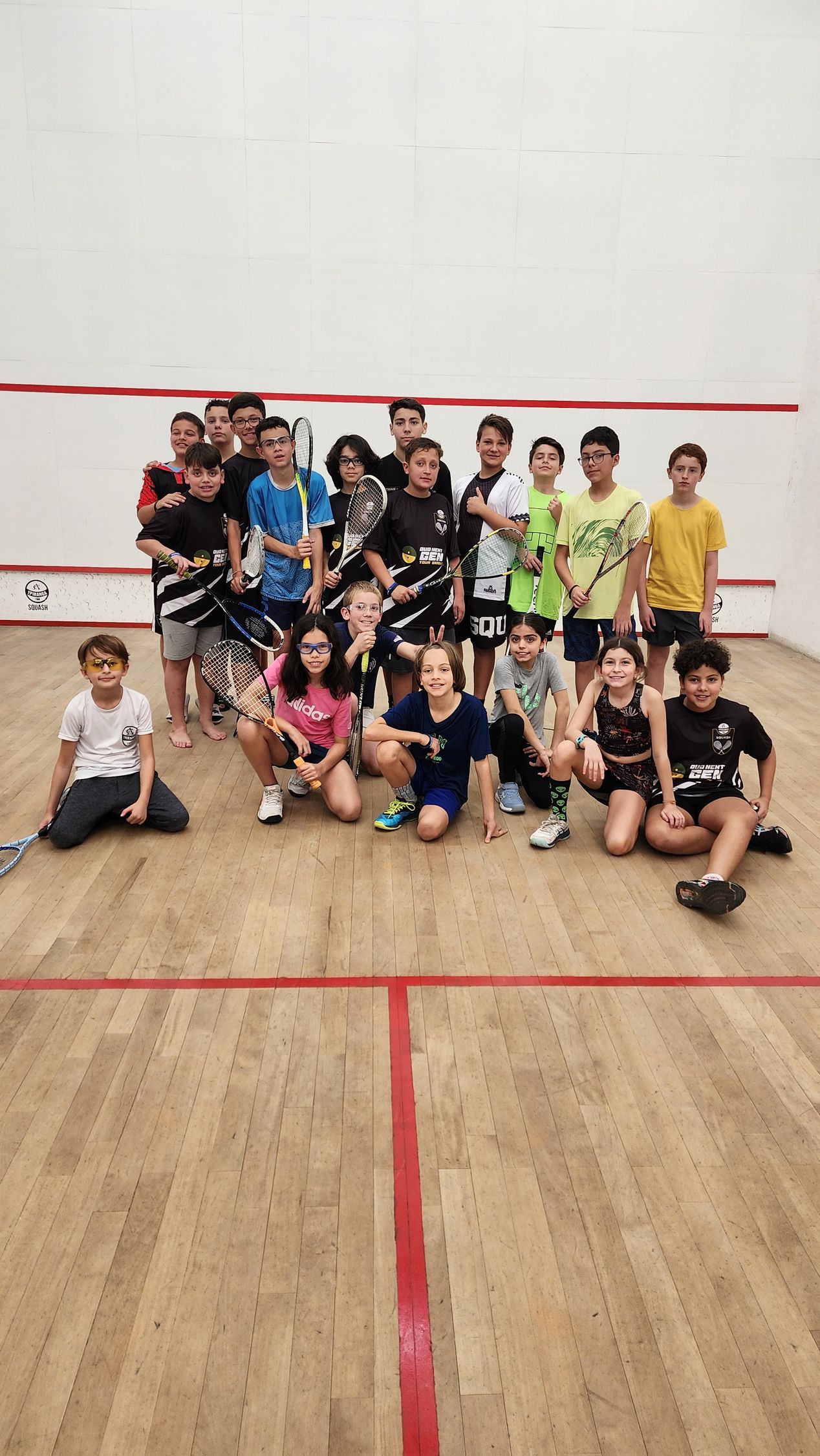 Um grupo de jovens está posando para uma foto em uma quadra de squash.
