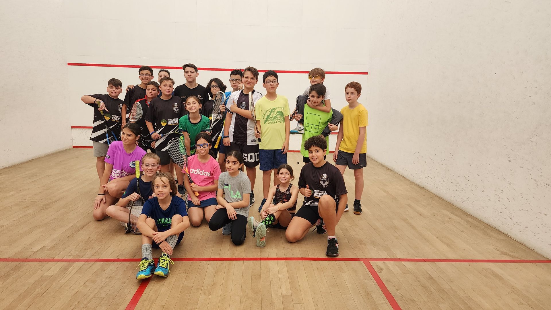 Um grupo de crianças está posando para uma foto em uma quadra de squash.
