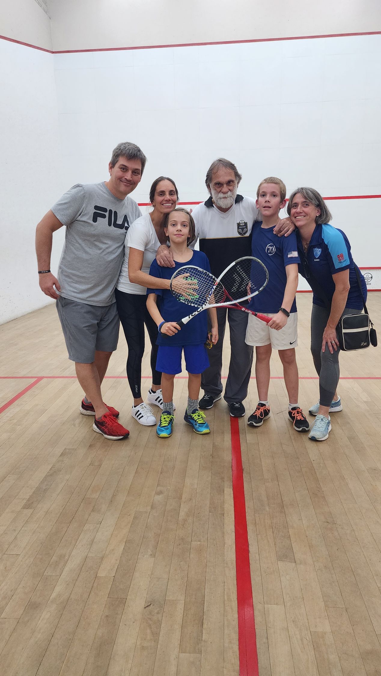 Um grupo de pessoas está posando para uma foto em uma quadra de squash.