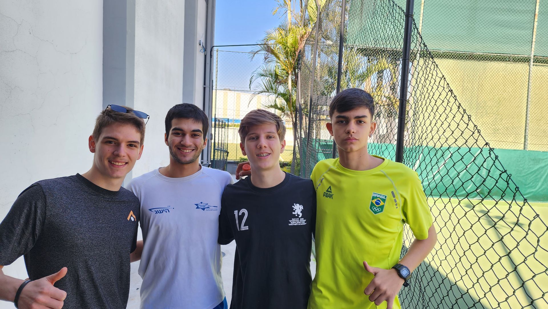 Um grupo de jovens está posando para uma foto em frente a uma quadra de tênis.