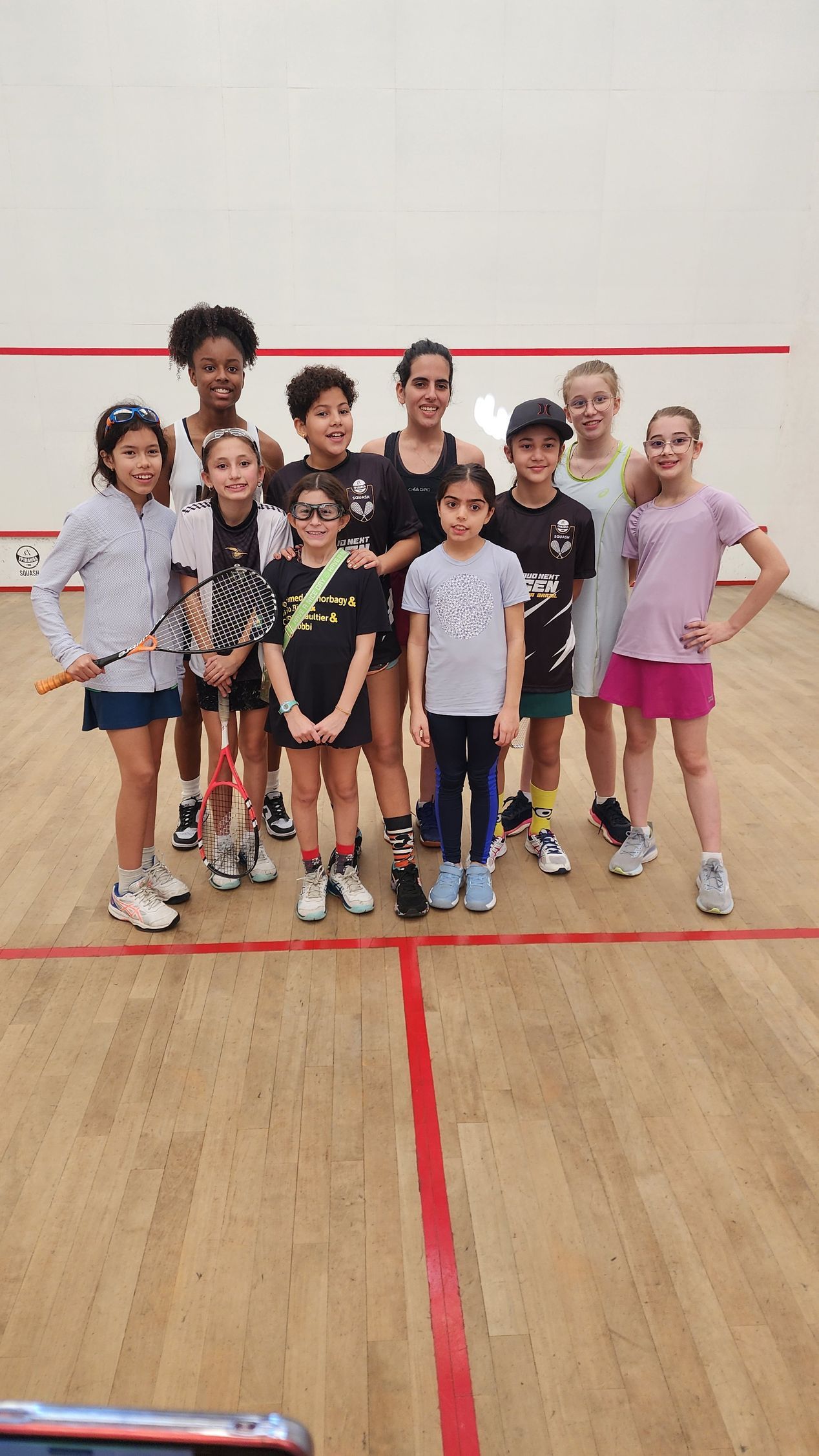 Um grupo de meninas está posando para uma foto em uma quadra de squash.