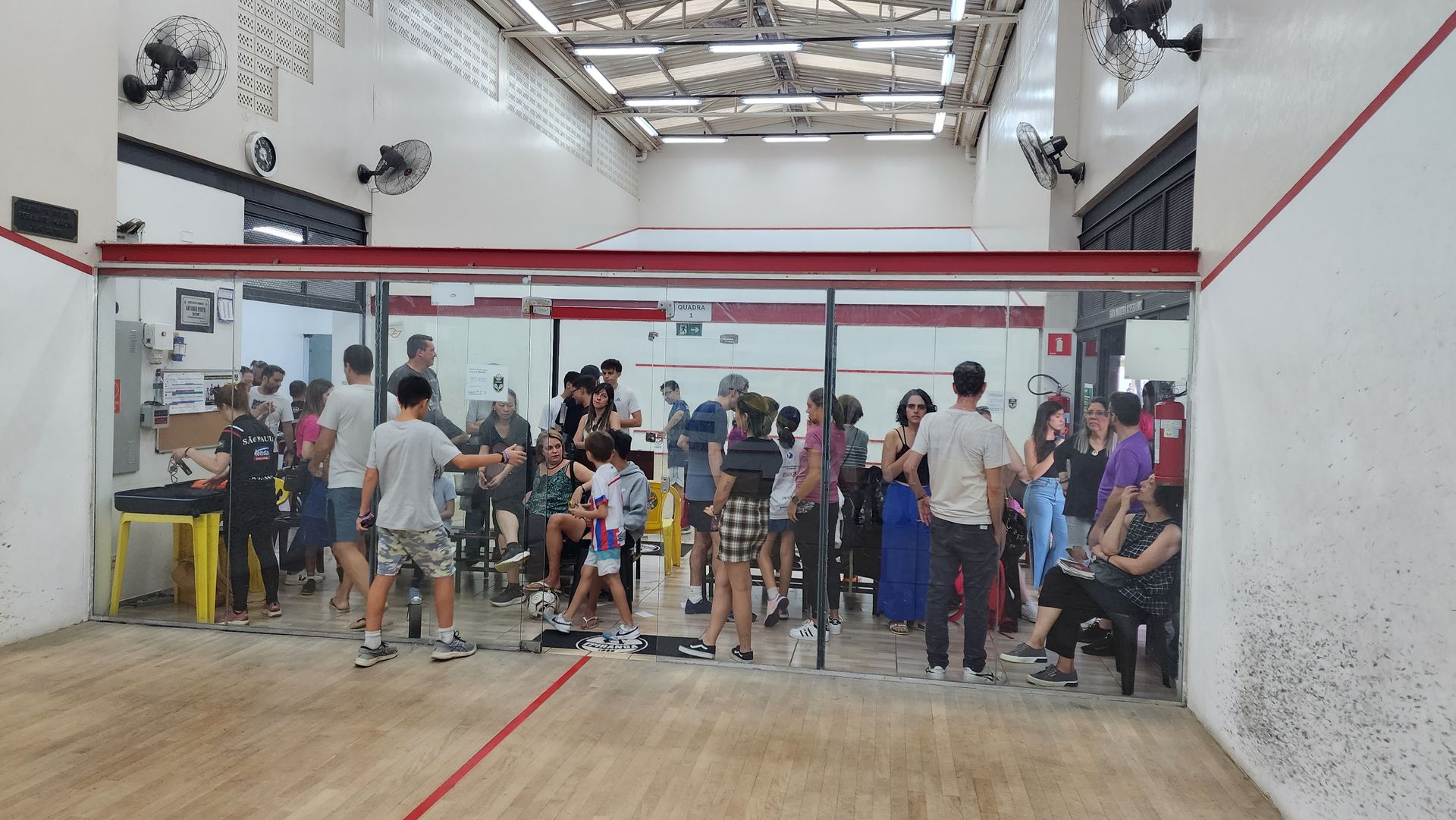 Um grupo de pessoas está em volta de uma quadra de squash.