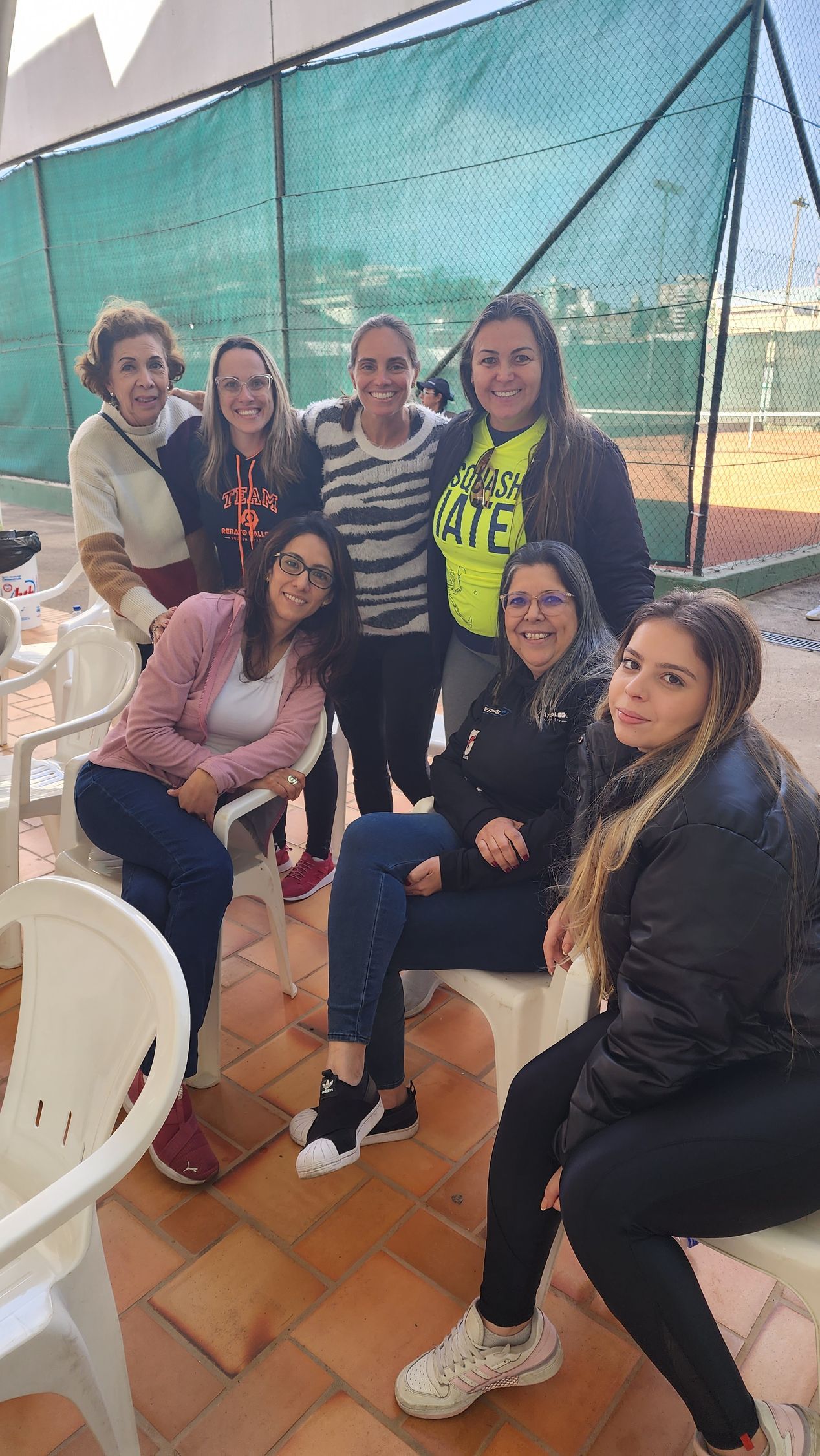 Um grupo de mulheres está posando para uma foto sentadas em mesas e cadeiras.