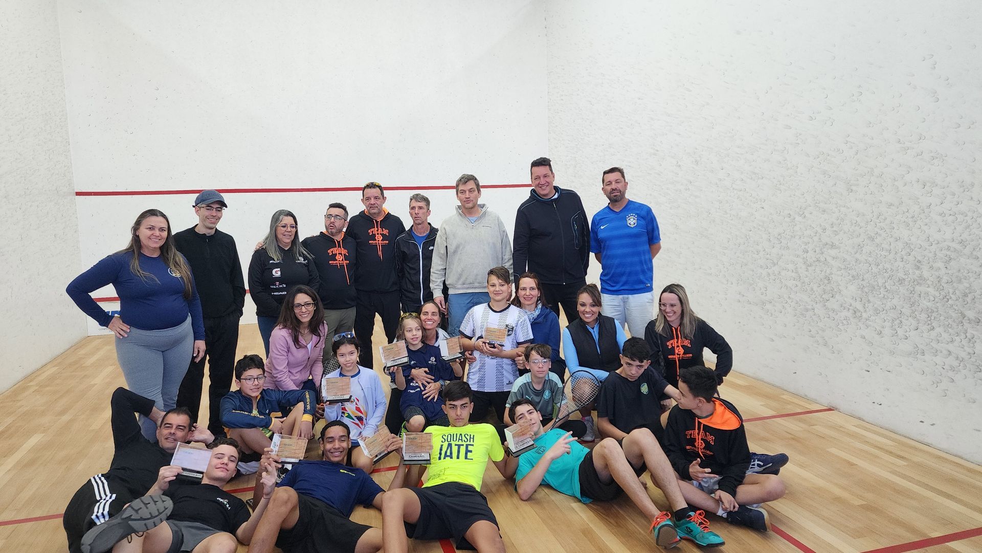 Um grupo de pessoas está posando para uma foto em uma quadra de squash.