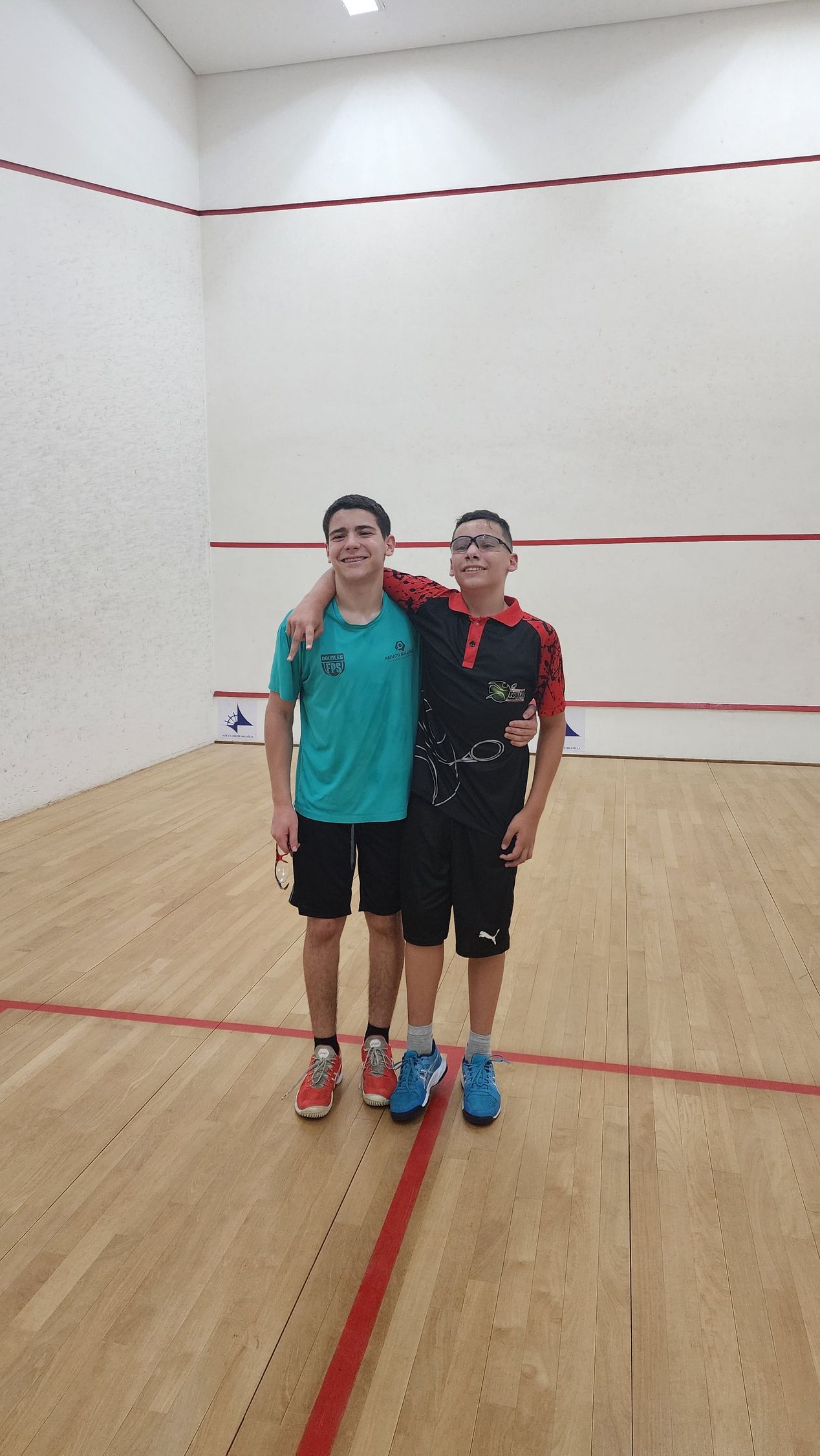 Dois homens estão posando para uma foto em uma quadra de squash.