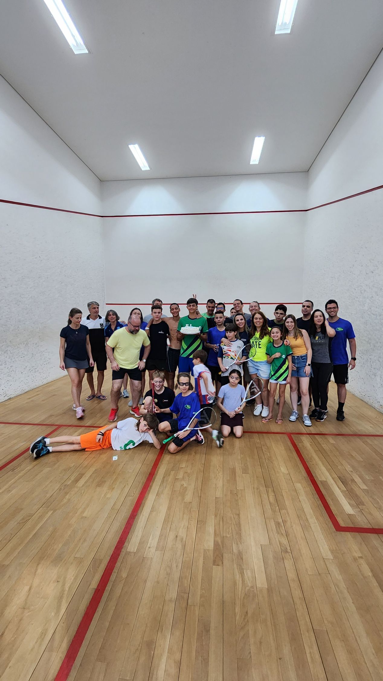 Um grupo de pessoas está posando para uma foto em uma quadra de squash.