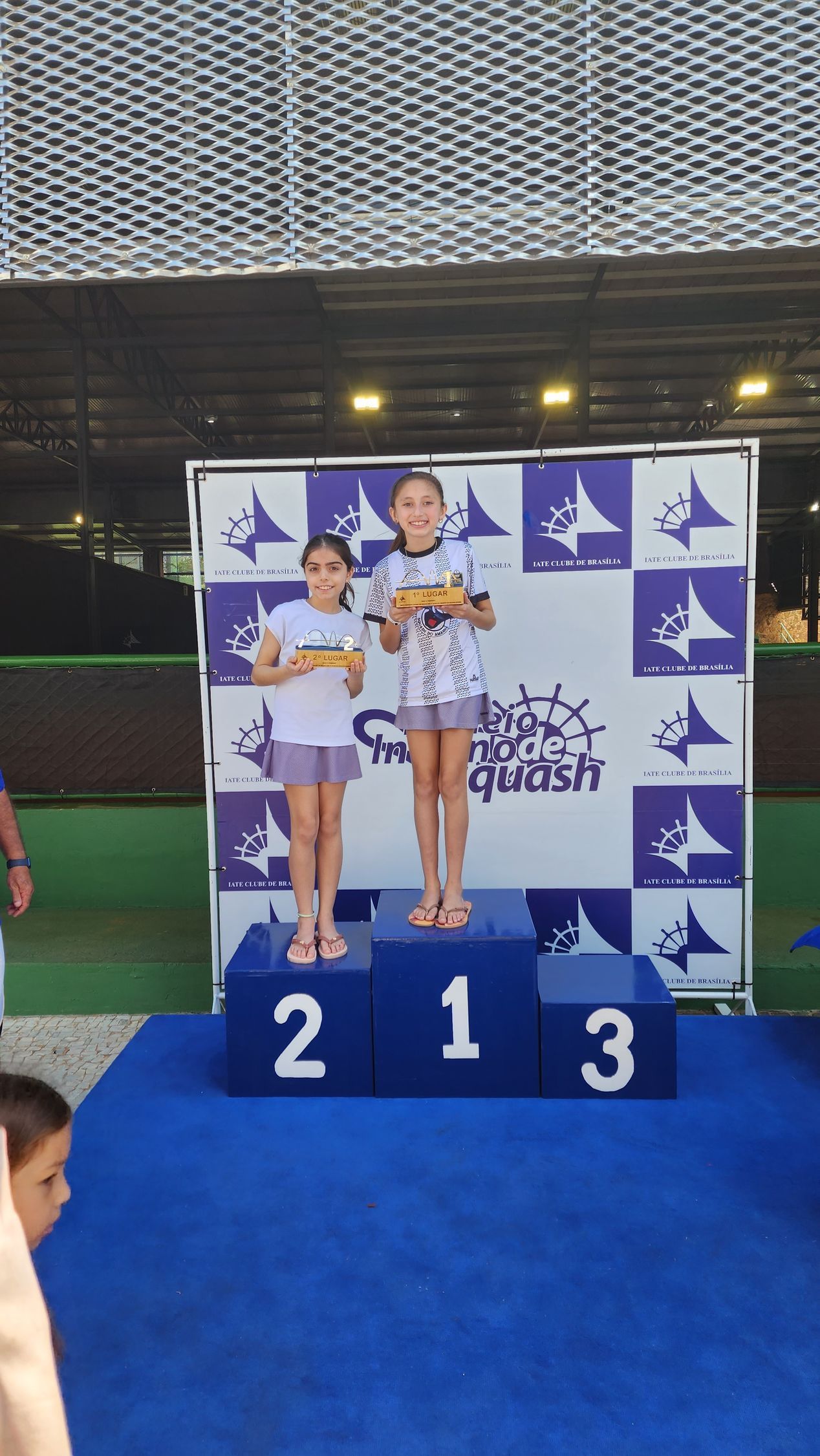 Duas meninas em pé em um pódio com os números 2 e 3