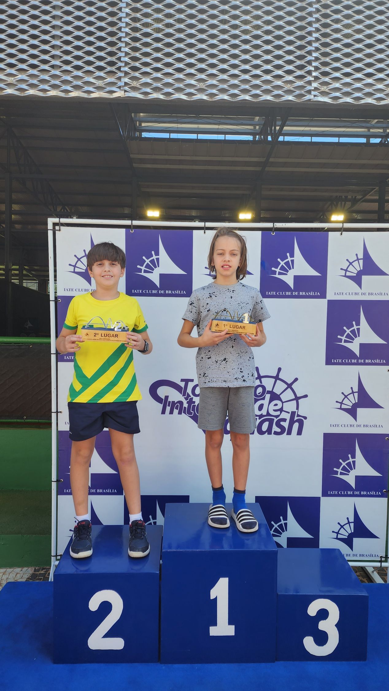 Dois meninos em pé em um pódio com os números 2 e 3