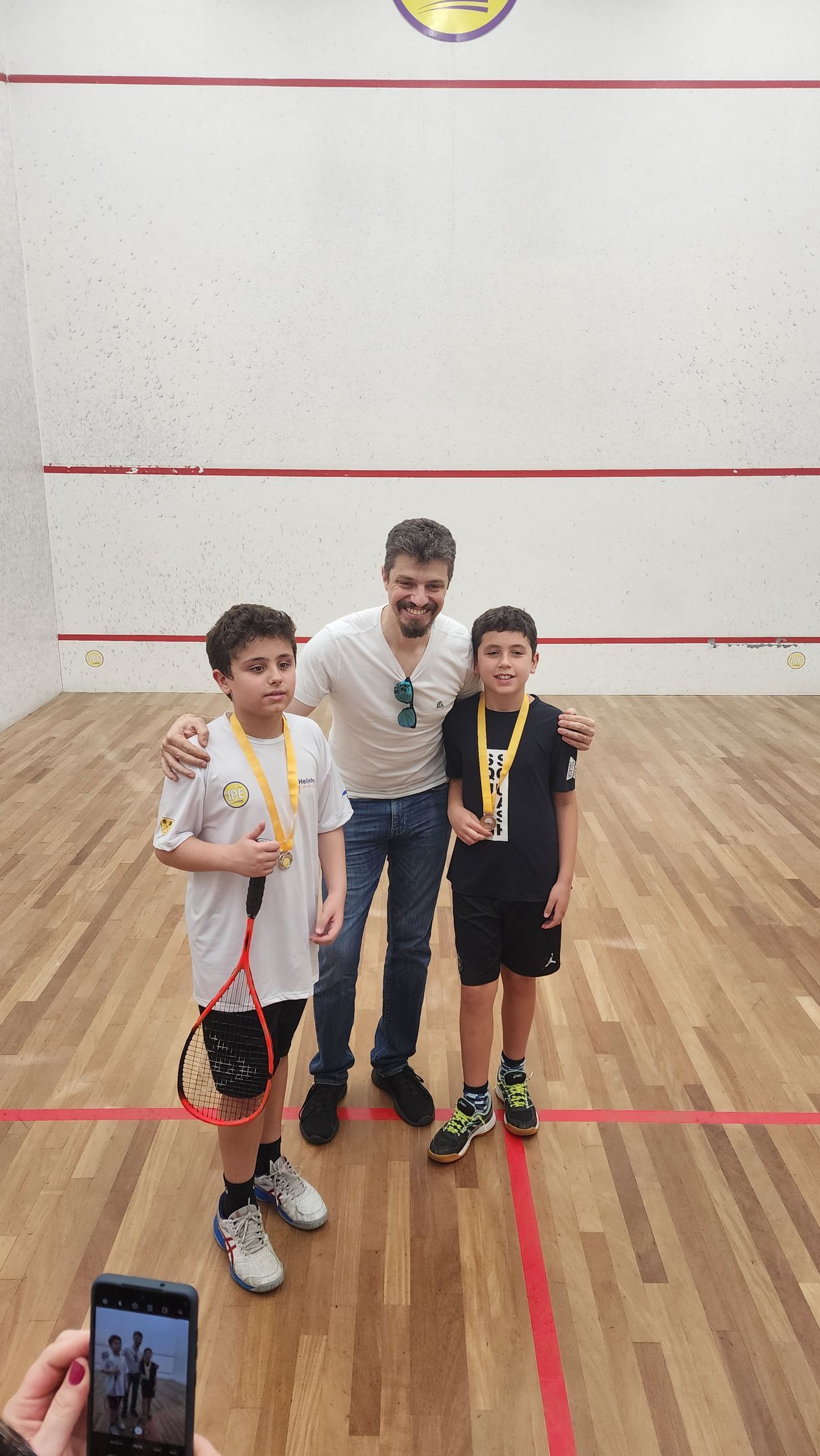Um homem e dois meninos estão posando para uma foto em uma quadra de squash.