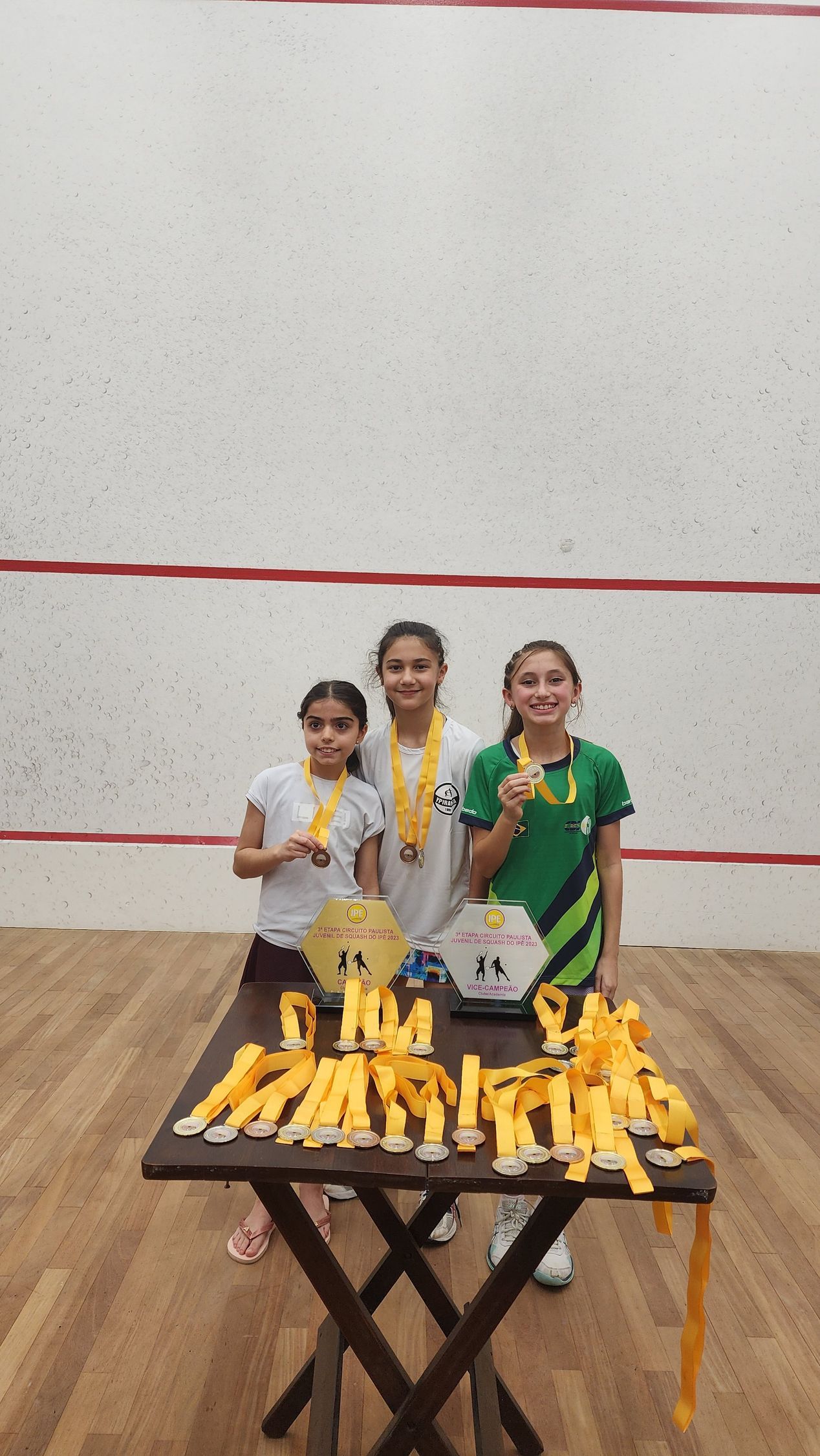 Três jovens estão de pé em frente a uma mesa com medalhas sobre ela.