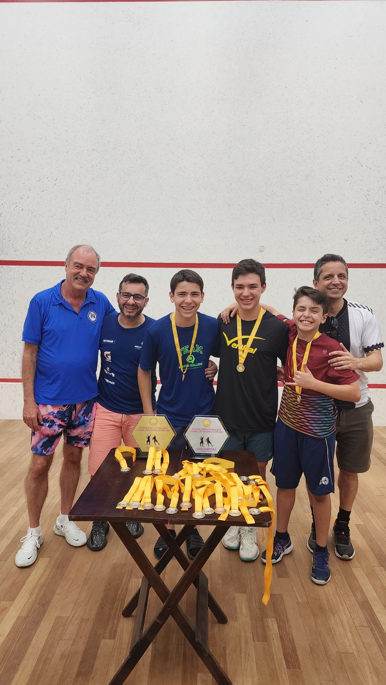 Um grupo de homens está em volta de uma mesa com troféus sobre ela.