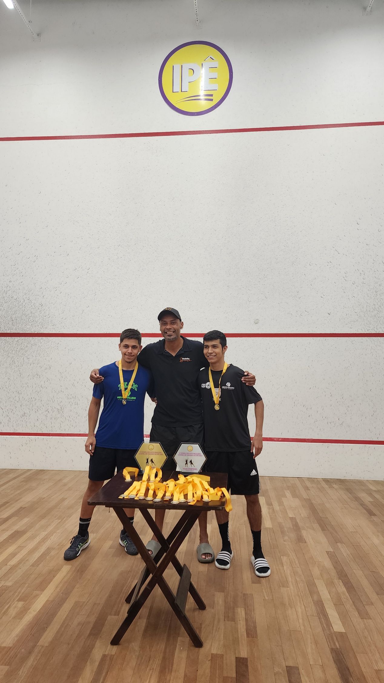 Três homens estão posando para uma foto em uma quadra de squash.