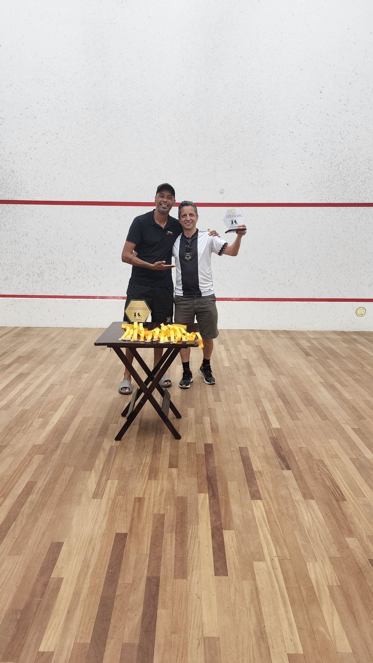 dois homens posam para uma foto em uma quadra de squash.