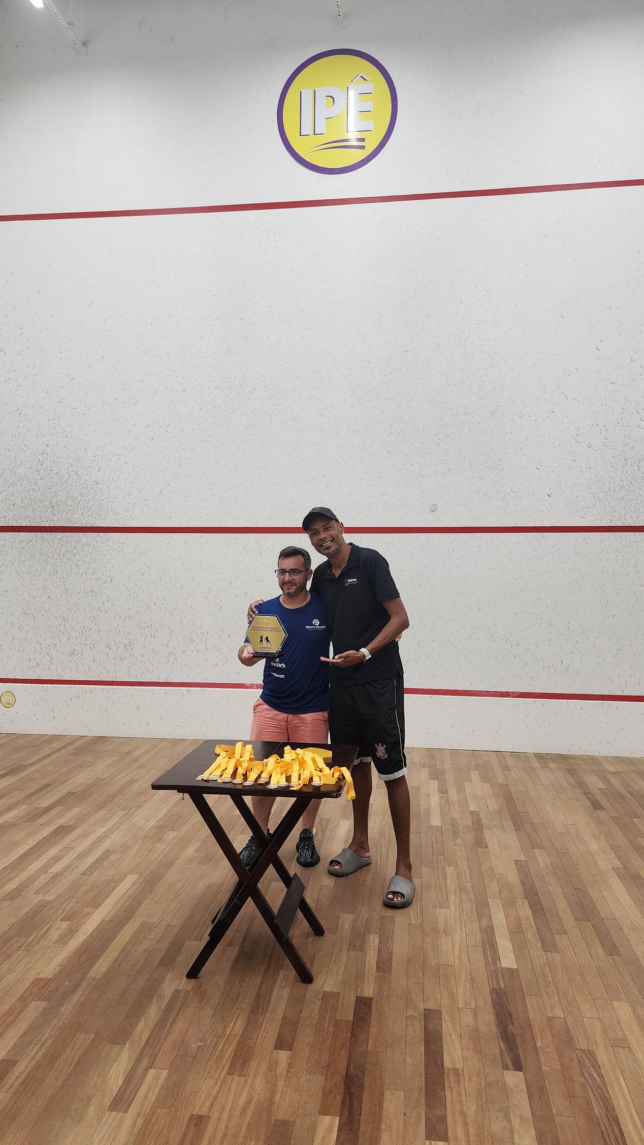 dois homens estão próximos um do outro em uma quadra de squash segurando troféus.