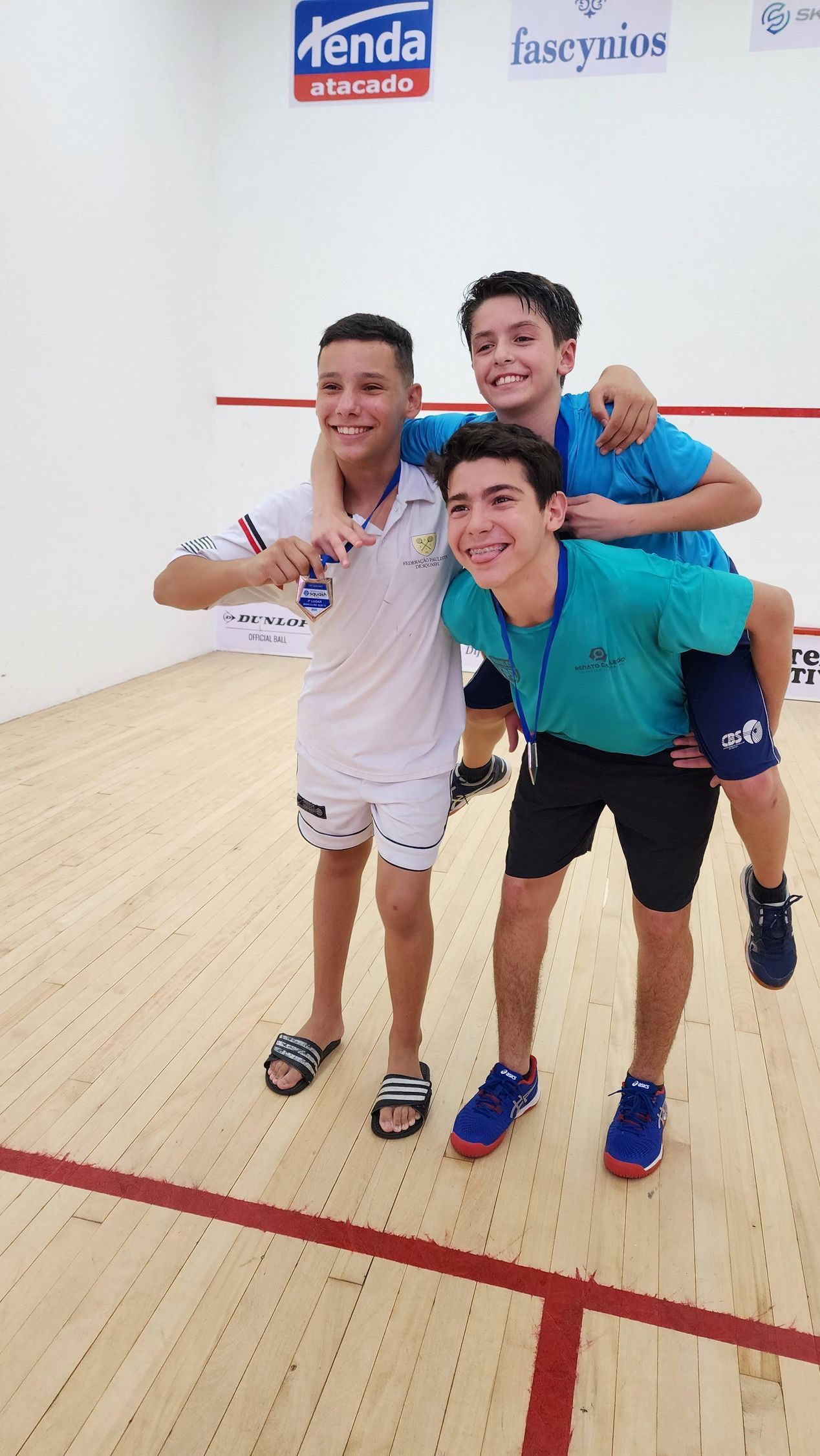 Três jovens estão posando para uma foto em uma quadra de squash.