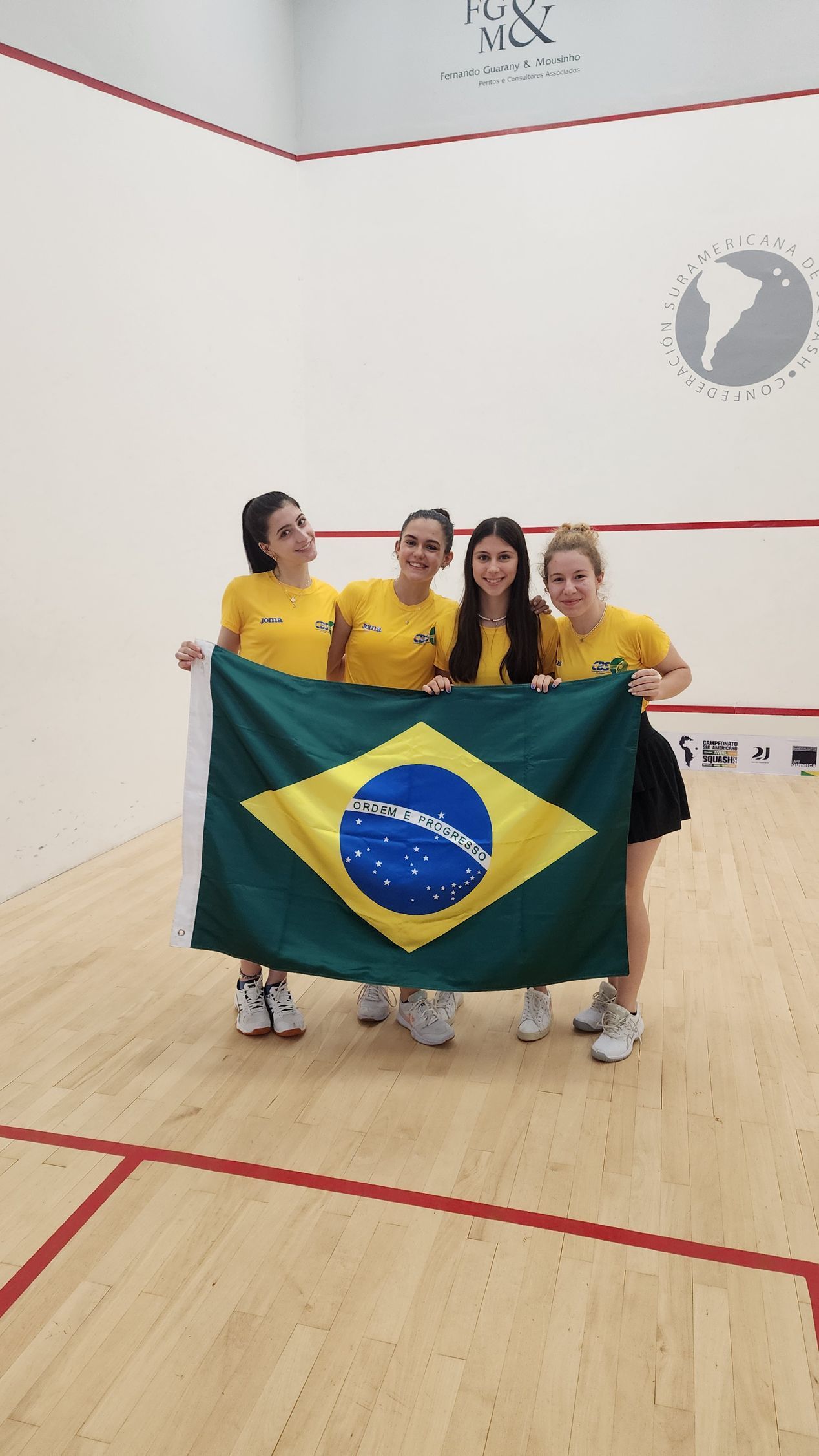 um grupo de mulheres segurando uma bandeira brasileira em uma quadra de squash