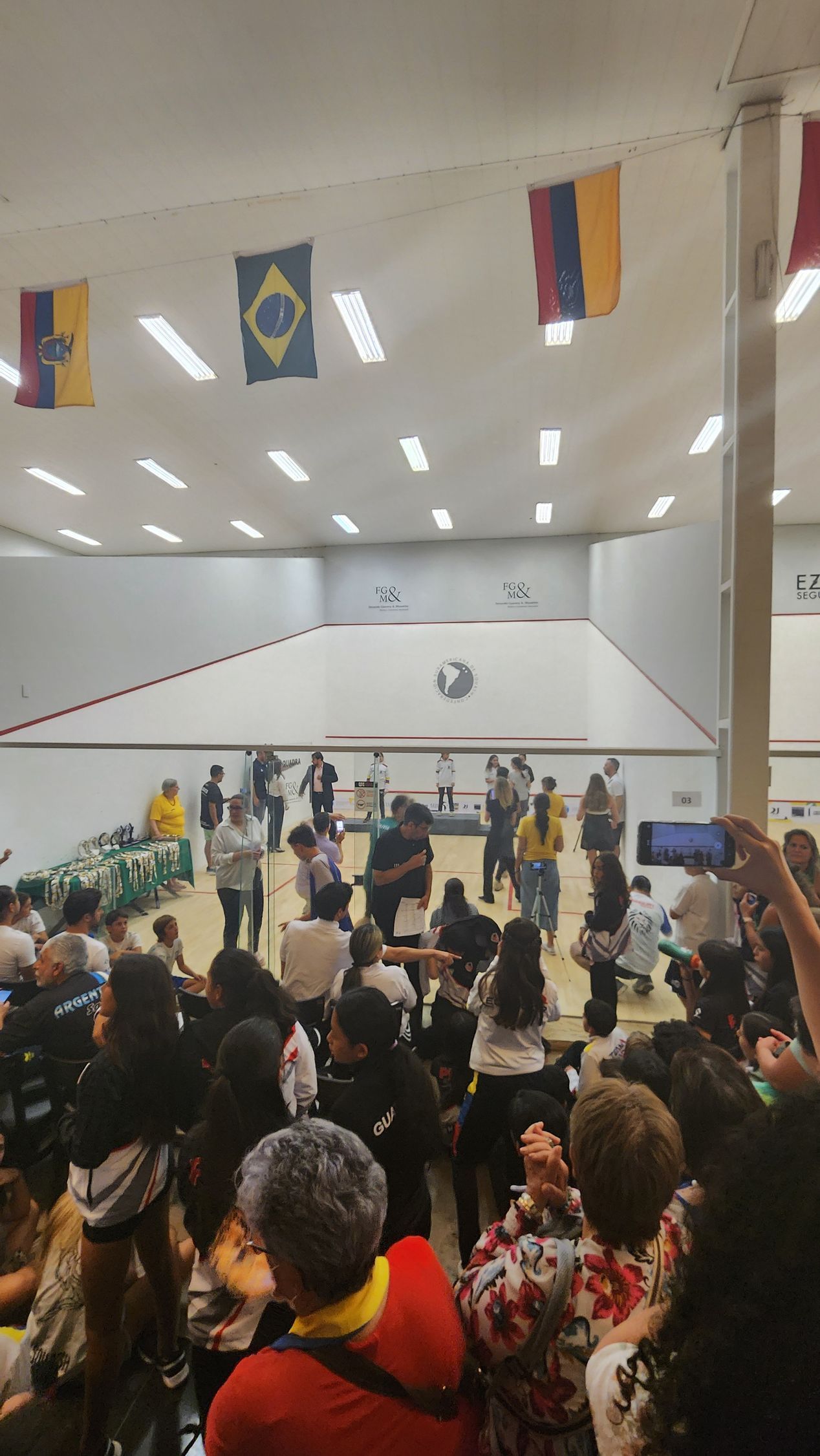 um grande grupo de pessoas está reunido em uma sala com bandeiras penduradas no teto.