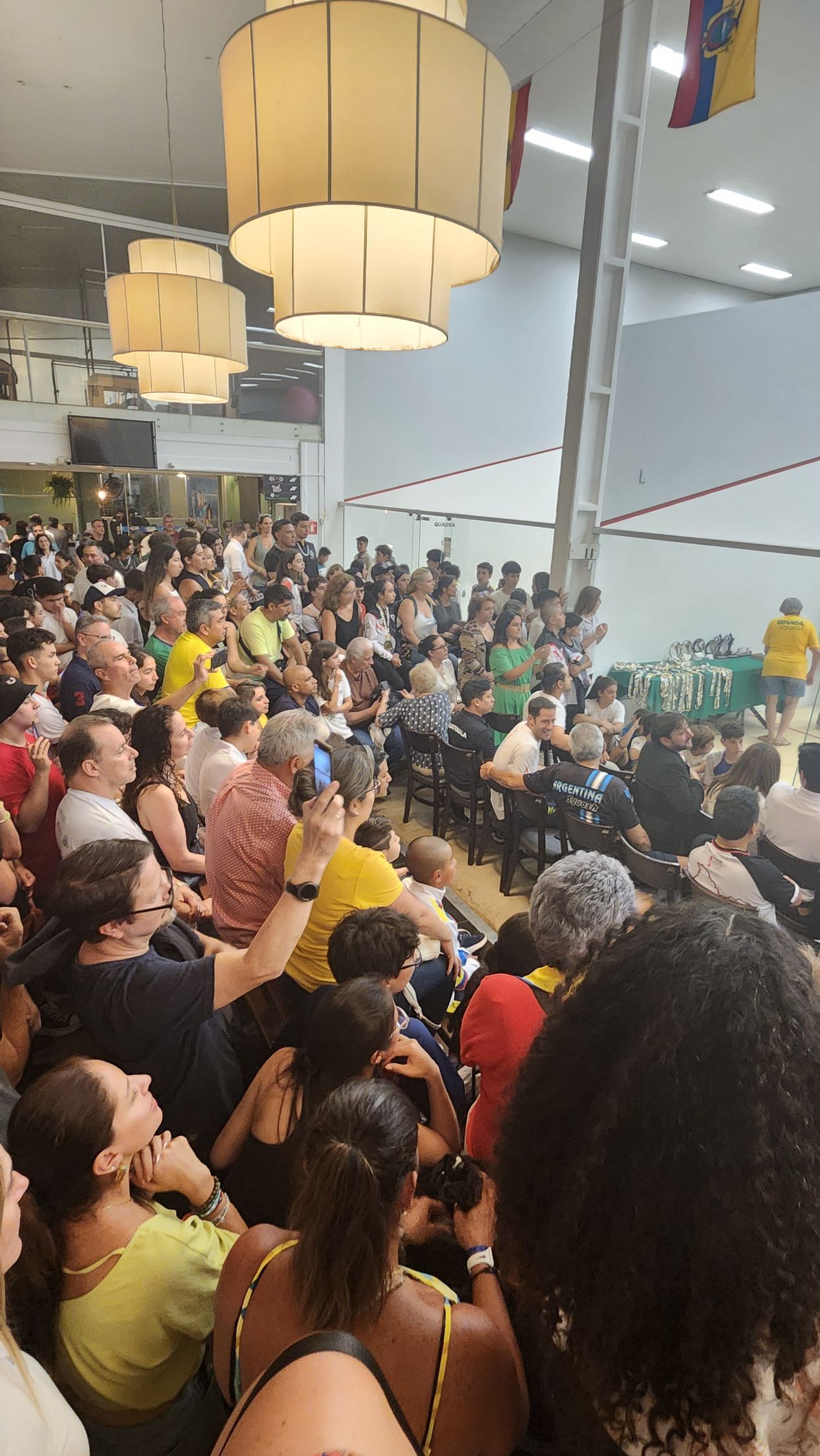 um grande grupo de pessoas está sentado em uma sala assistindo a uma luta de boxe.