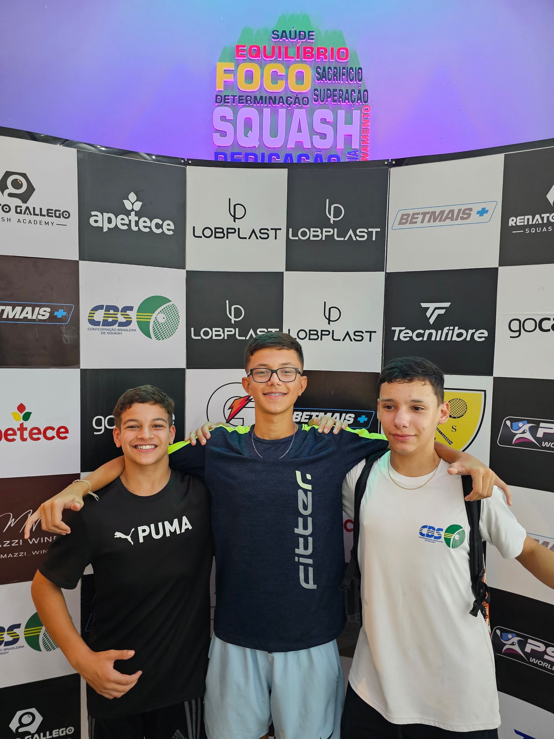 Três jovens estão posando para uma foto em frente a uma parede com logotipos.