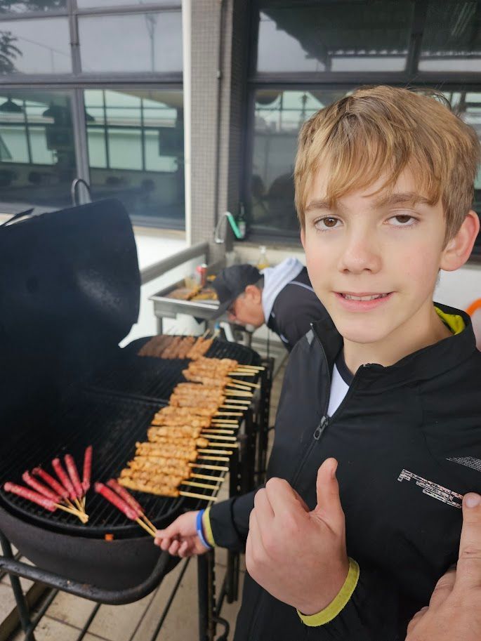 Um menino está dando um sinal de positivo na frente de uma grelha