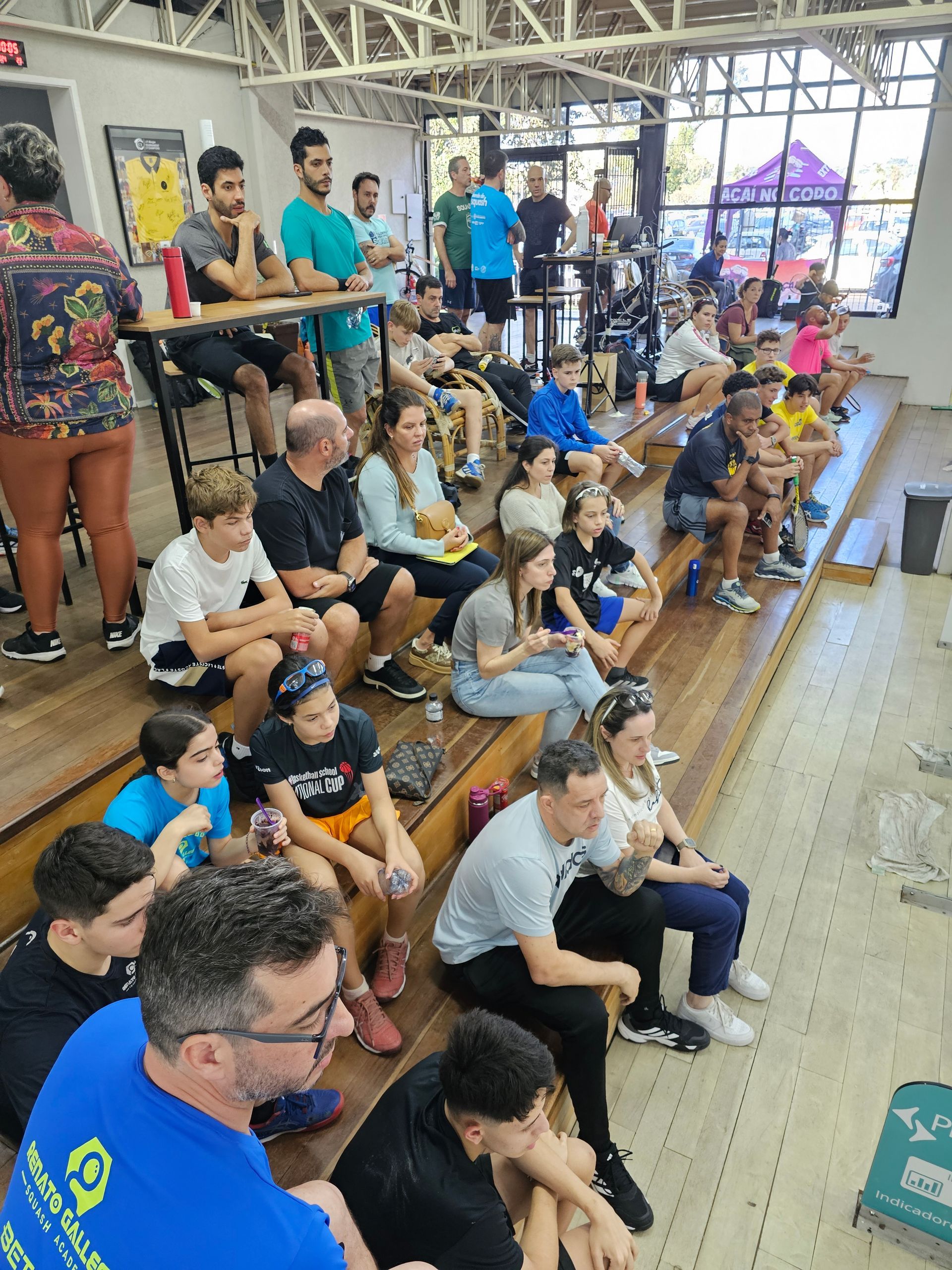 Um grupo de pessoas está sentado em um banco de madeira em uma sala.