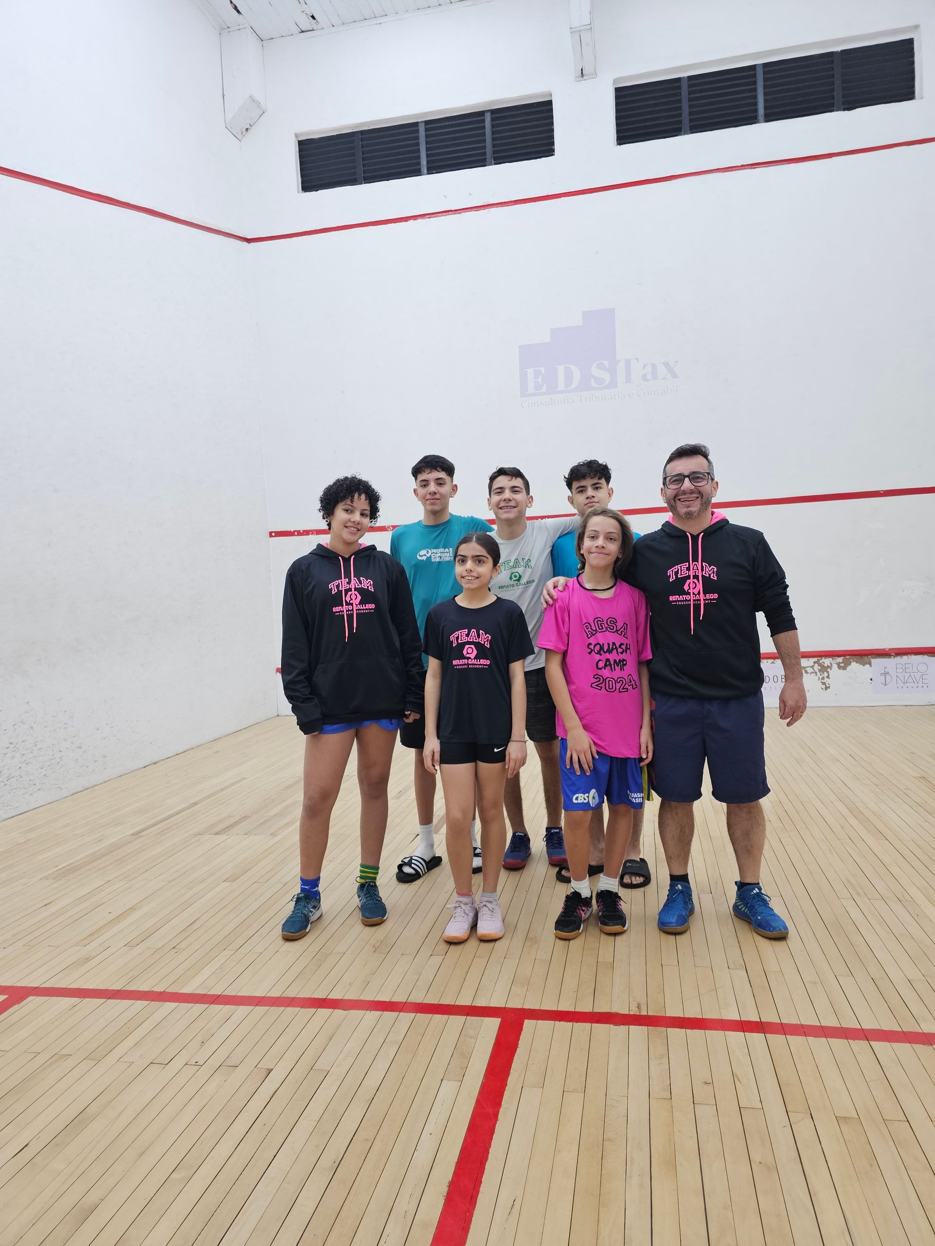 Um grupo de pessoas está posando para uma foto em uma quadra de squash