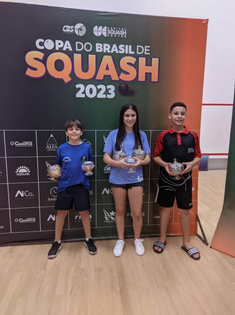 Três pessoas estão em frente a uma placa que diz copa do brasil de squash 2023.
