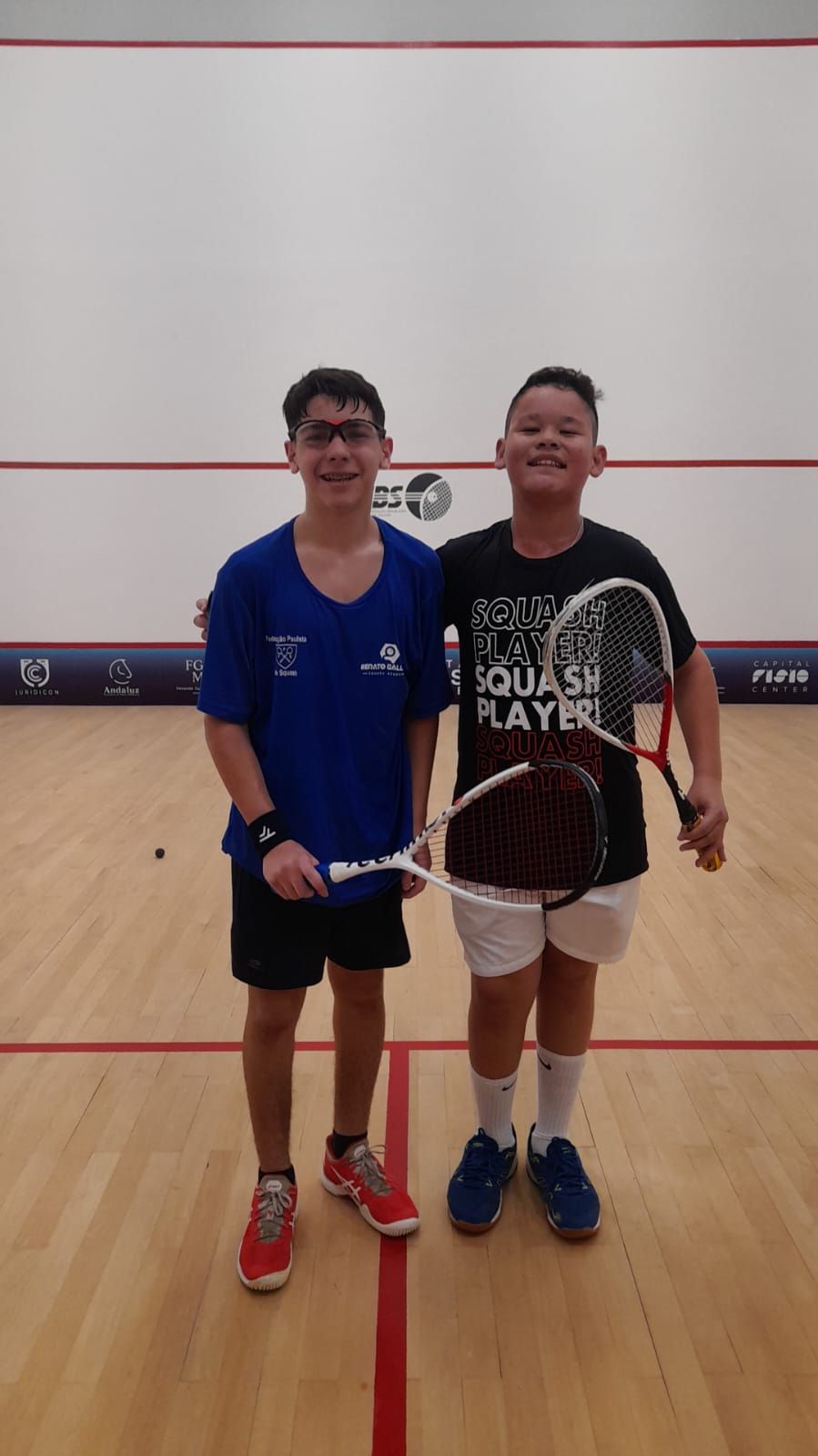 Dois jovens estão posando para uma foto em uma quadra de squash.
