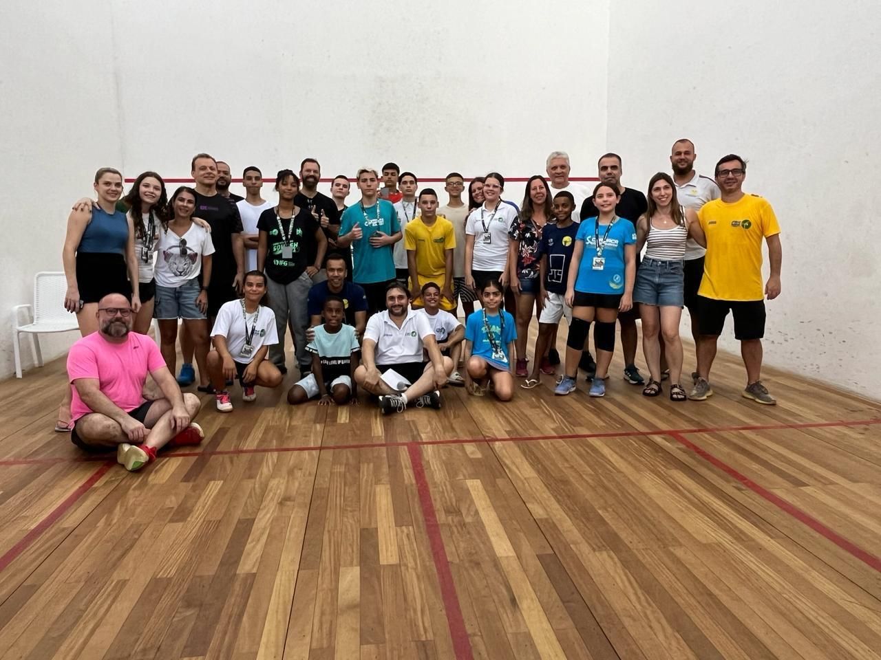 Um grupo de pessoas está posando para uma foto em uma quadra de squash.