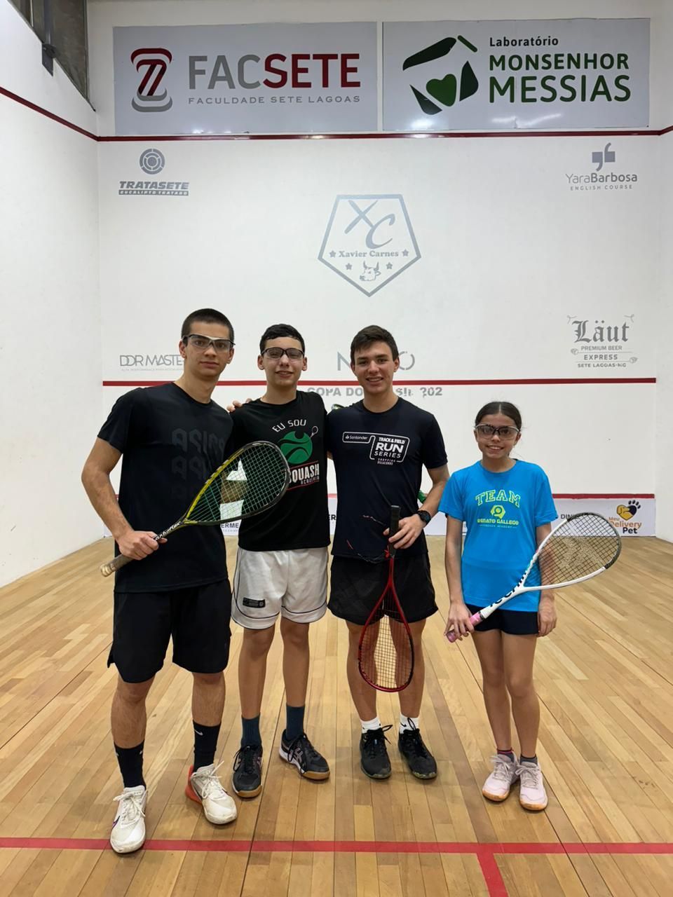 Um grupo de pessoas está posando para uma foto em uma quadra de squash