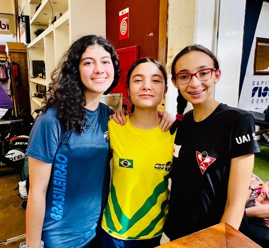 Três meninas estão posando para uma foto e uma delas está com uma blusa que diz brasileira