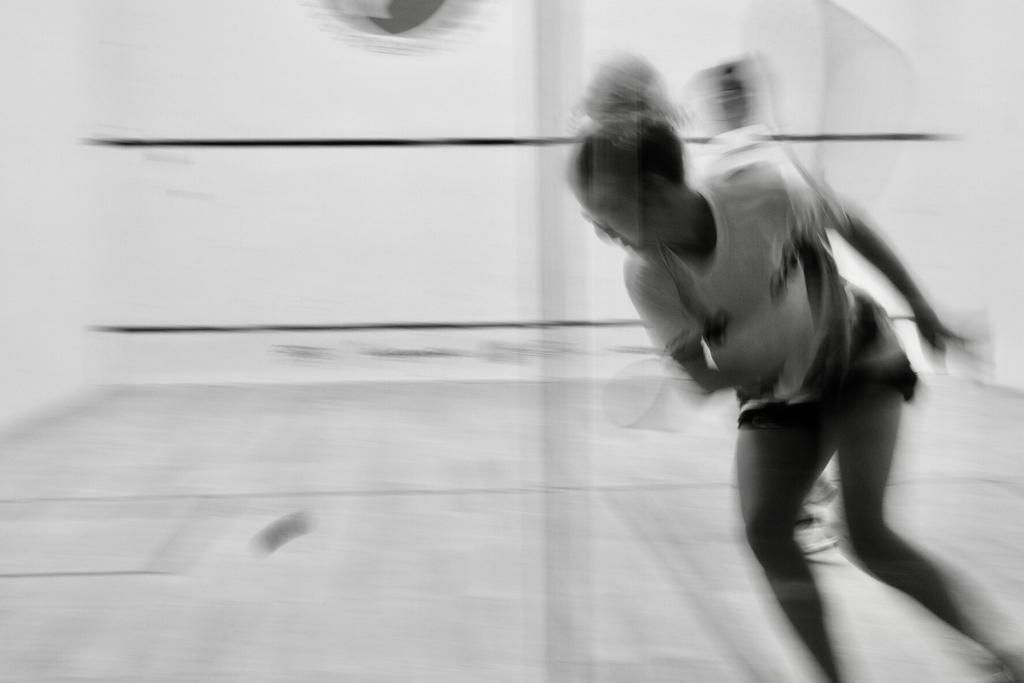 Uma mulher está jogando squash em uma quadra em uma foto em preto e branco.