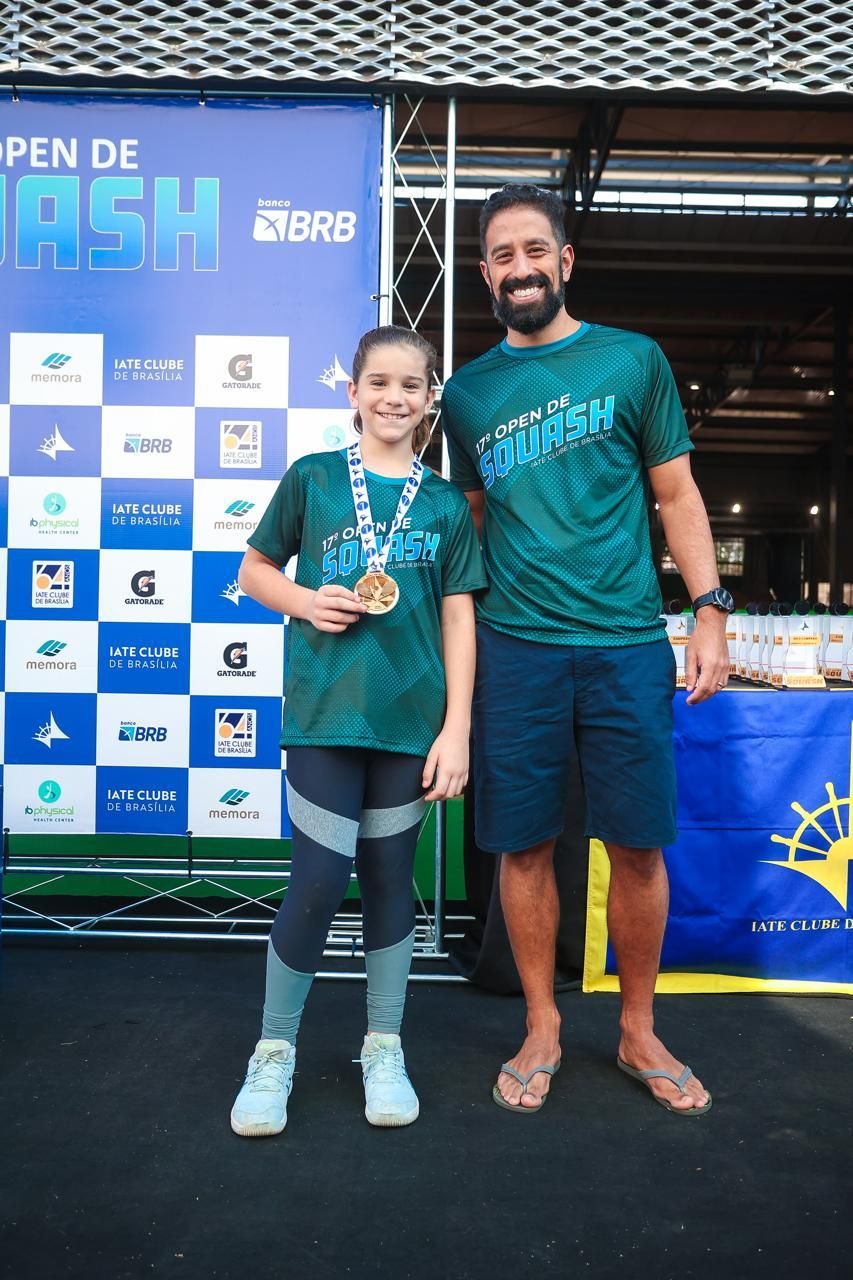 Um homem e uma menina estão de pé, um ao lado do outro, segurando medalhas.