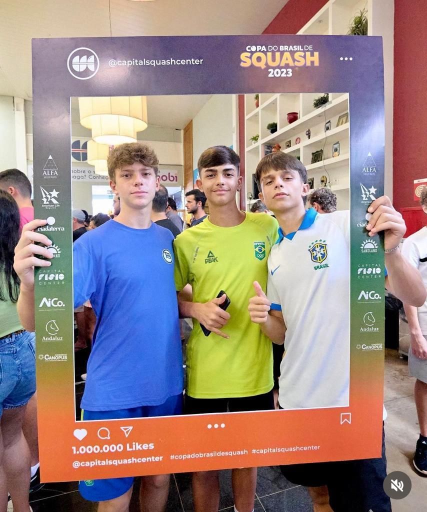 Três jovens estão de pé, um ao lado do outro, segurando uma moldura.