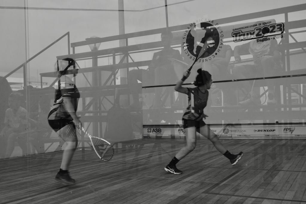 Duas mulheres estão jogando squash em uma quadra de madeira.