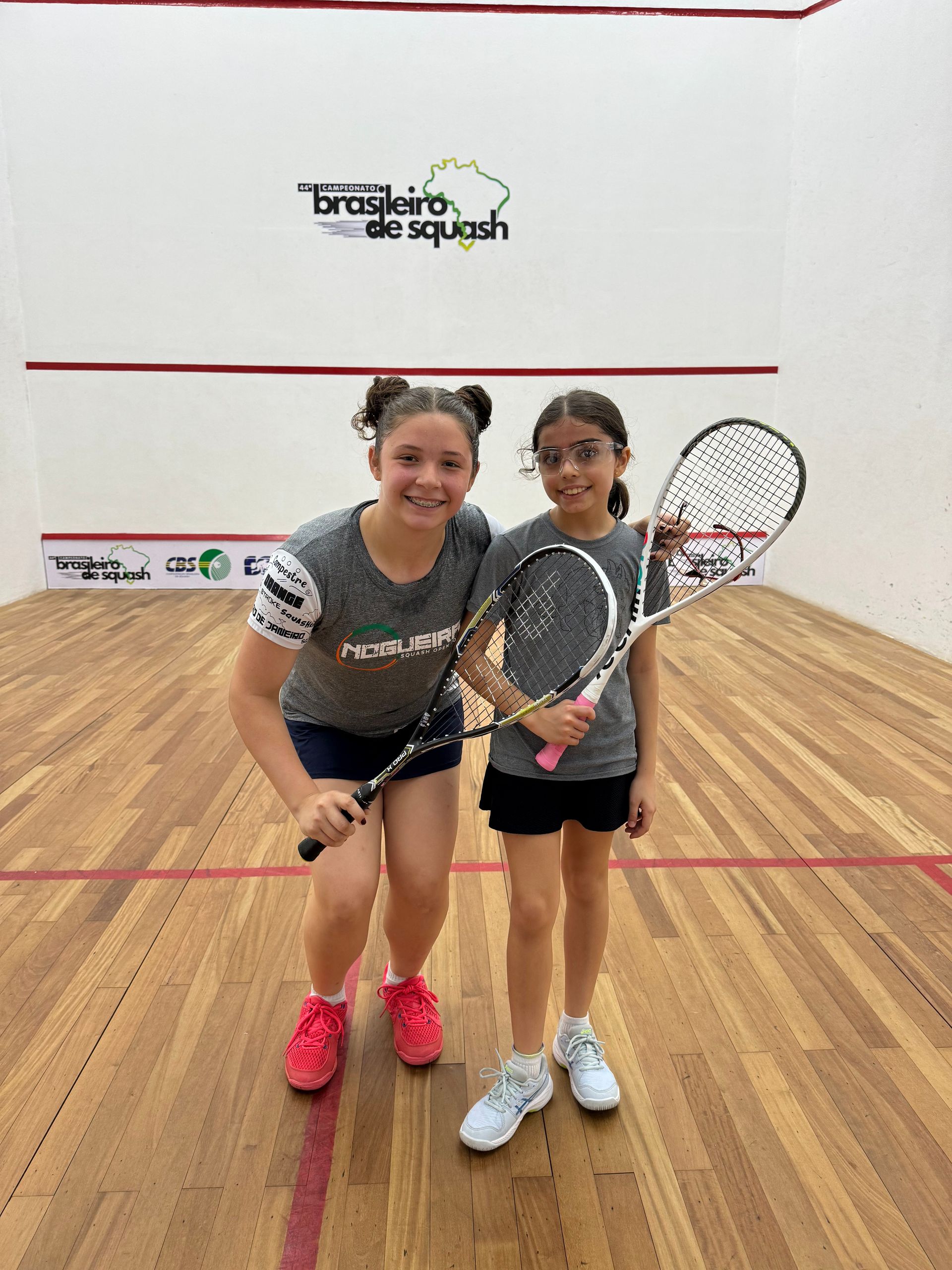 Duas jovens estão posando para uma foto em uma quadra de squash.