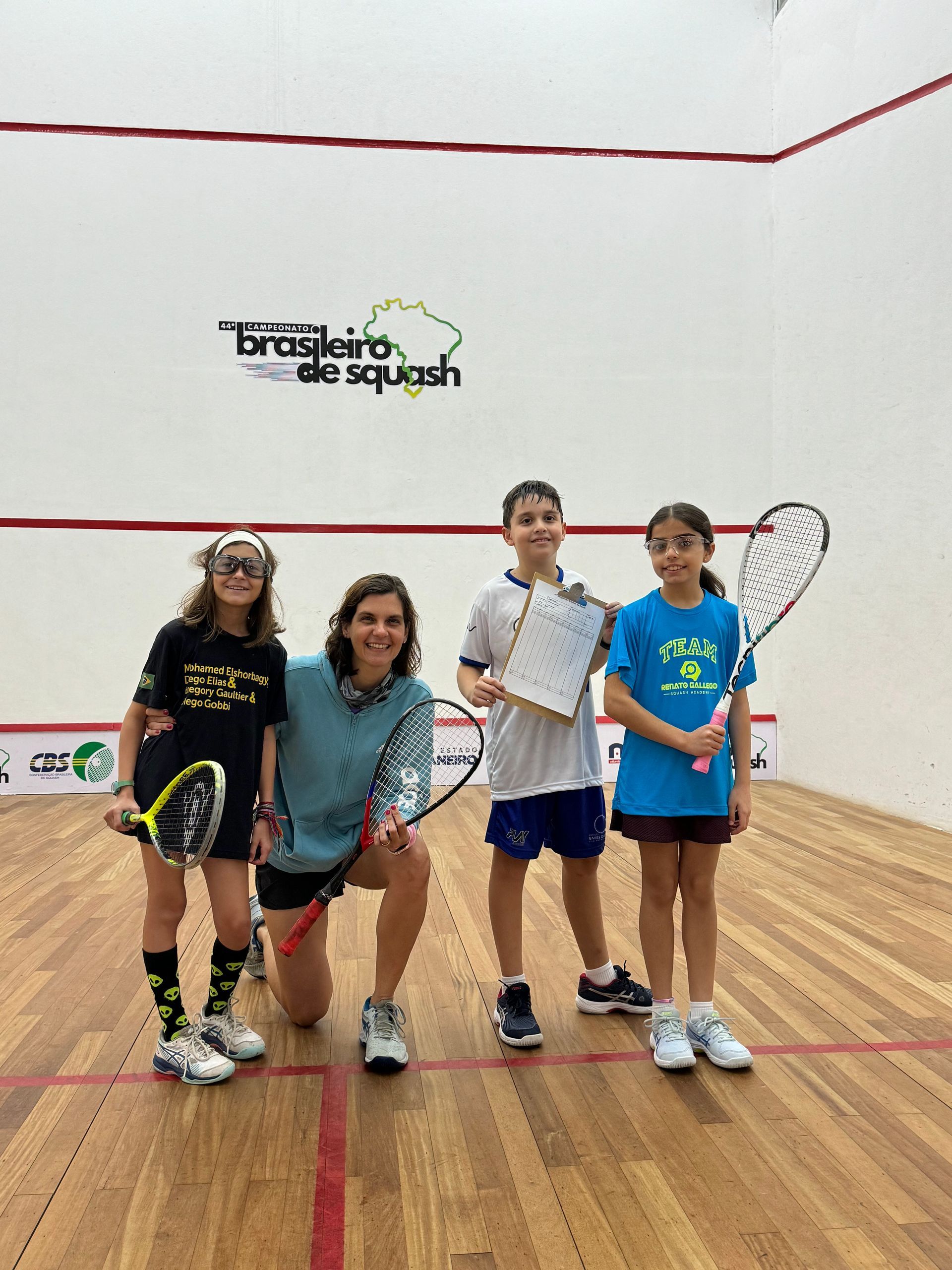 Um grupo de pessoas está posando para uma foto em uma quadra de squash.
