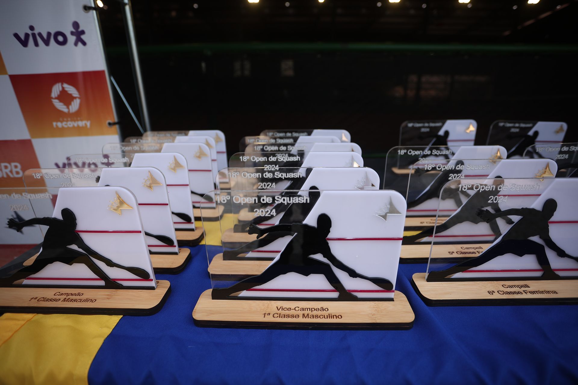 Um monte de troféus em uma mesa com uma placa da vivo ao fundo