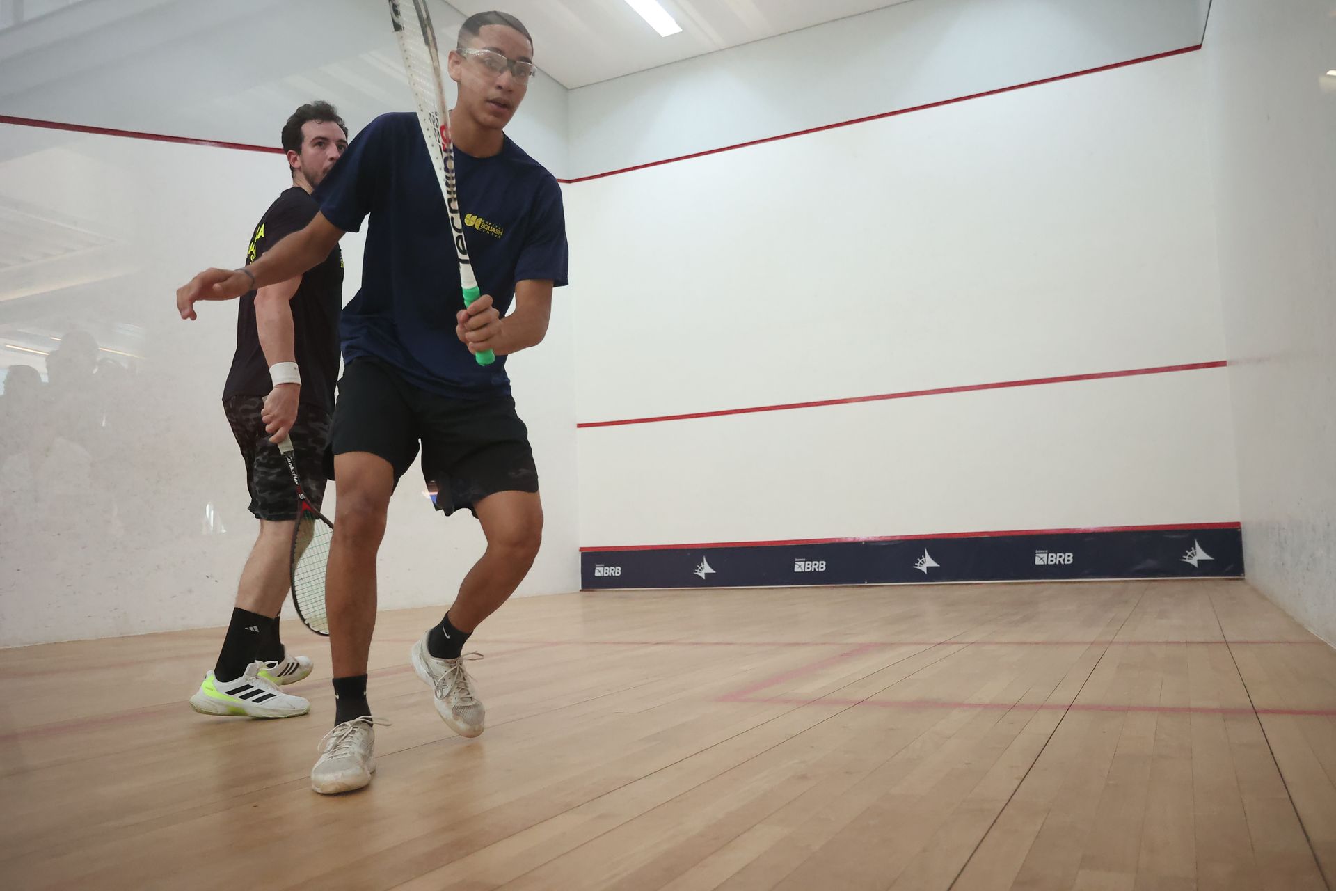 Dois homens estão jogando squash em uma quadra de madeira