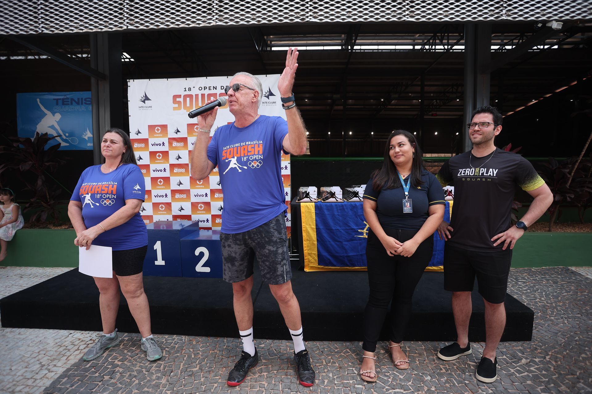 Um homem está falando em um microfone enquanto está ao lado de um grupo de pessoas.