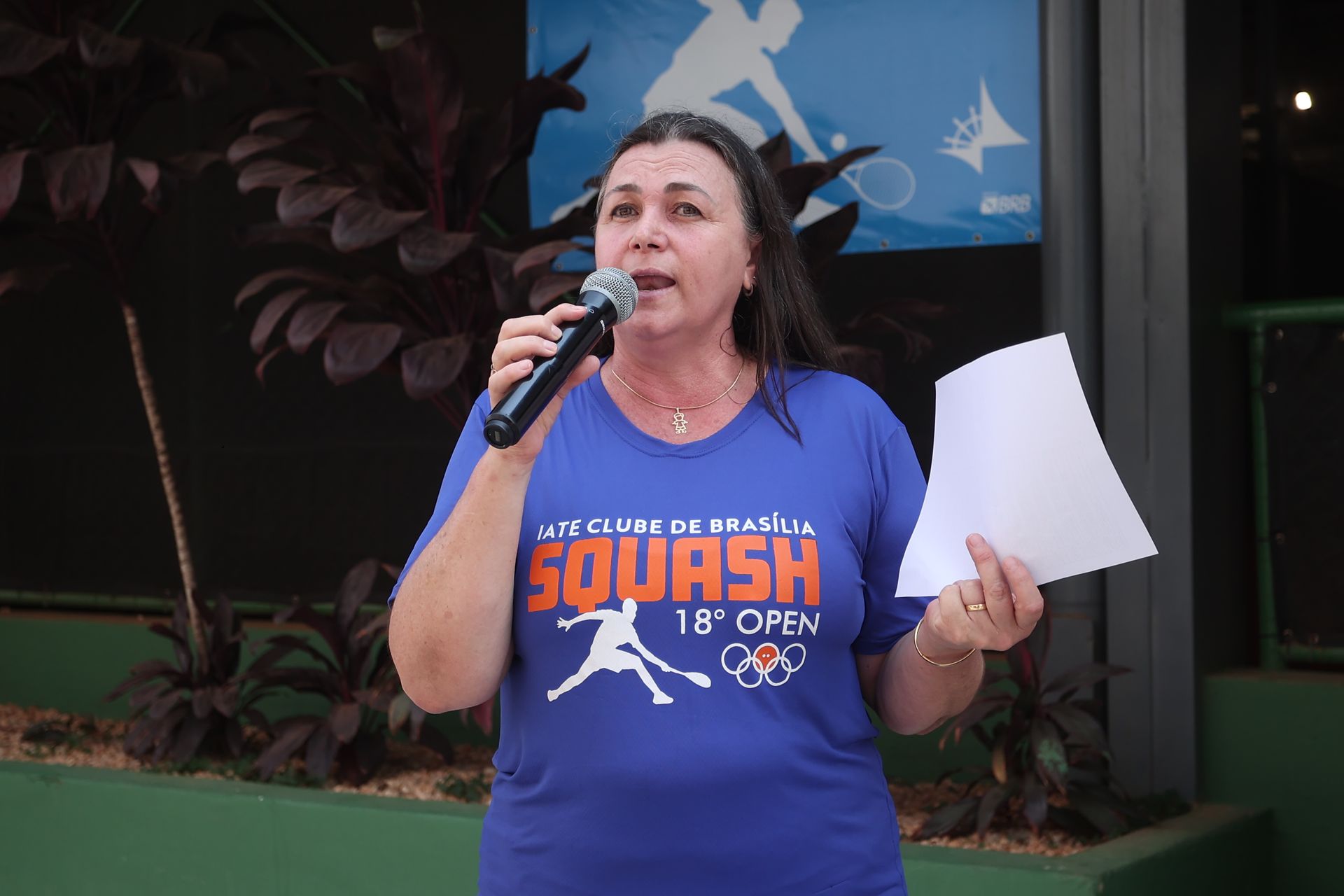 Uma mulher vestindo uma camisa azul que diz squash está falando em um microfone