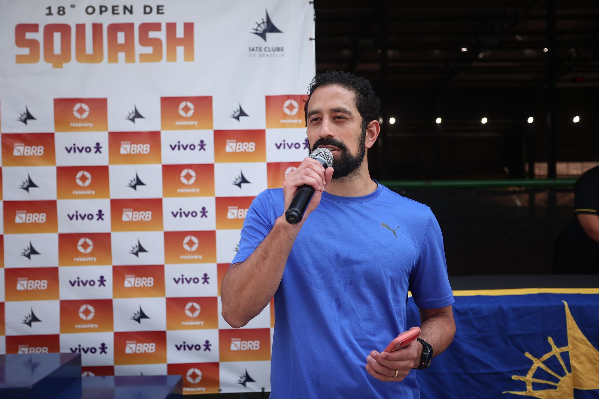 Um homem falando em um microfone em frente a uma placa que diz squash