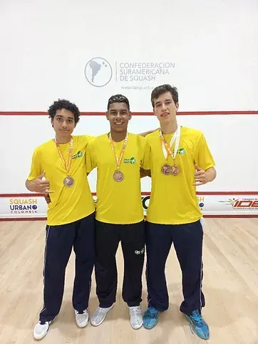 Três jovens vestindo camisas amarelas e medalhas estão posando para uma foto.