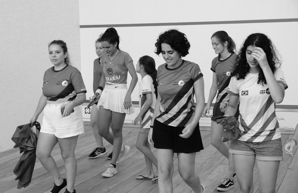 Um grupo de jovens mulheres caminha em fila sobre um piso de madeira.