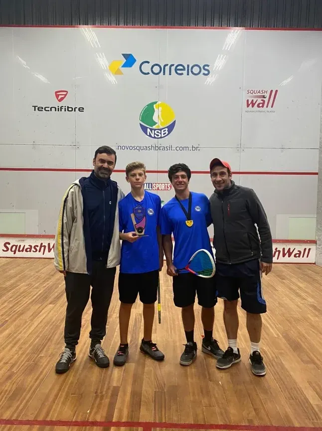 Um grupo de jovens está posando para uma foto em uma quadra de squash.